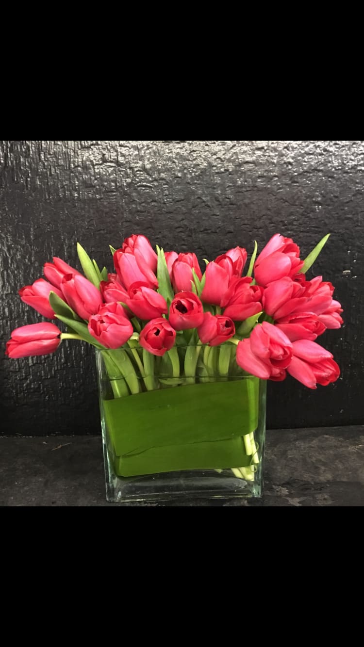 Pink tulips arranged in a clear glass vase with green wrap