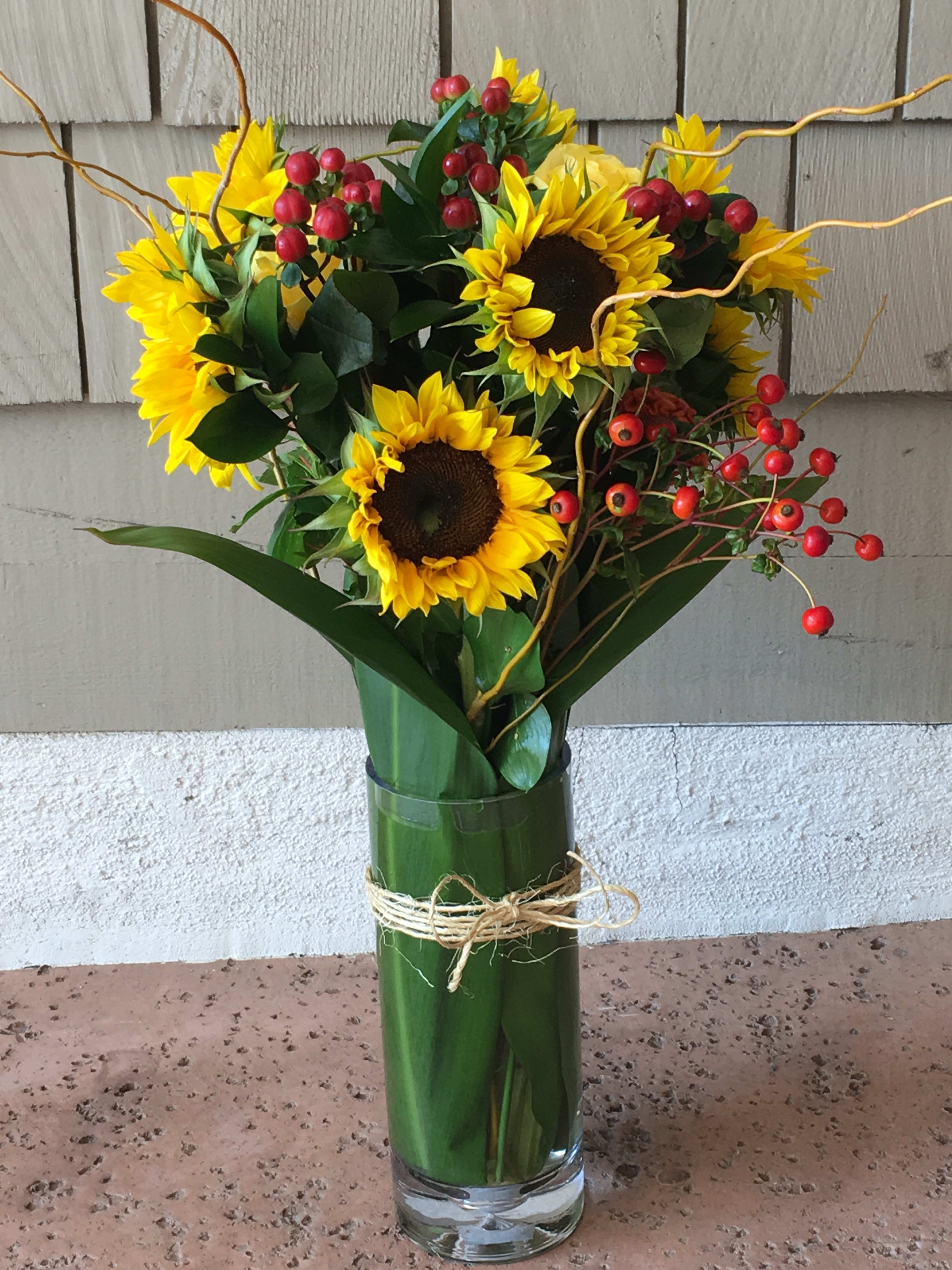 Sunflower bouquet in a glass vase with red berry accents