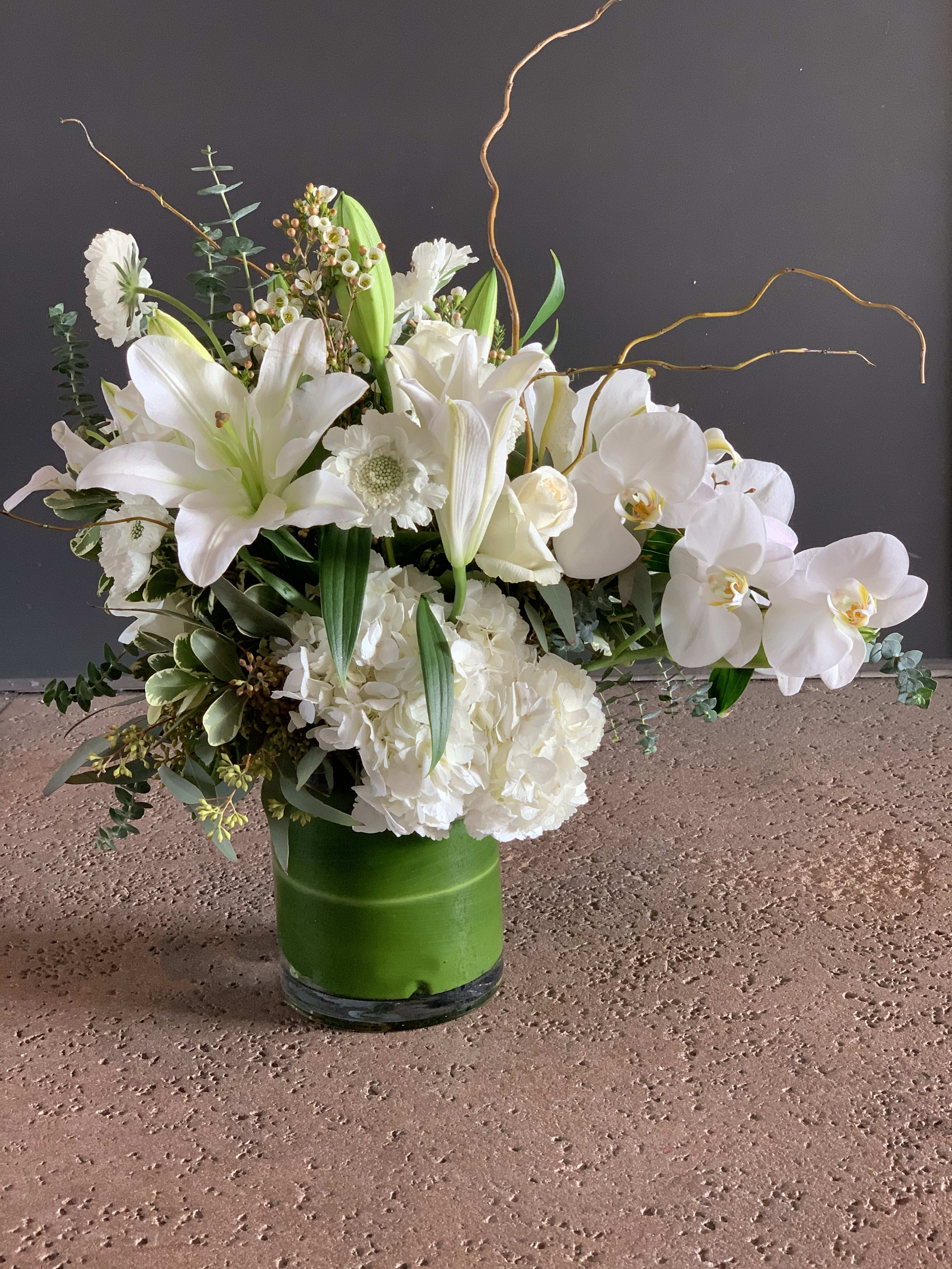 White lilies and orchids arranged in a green vase