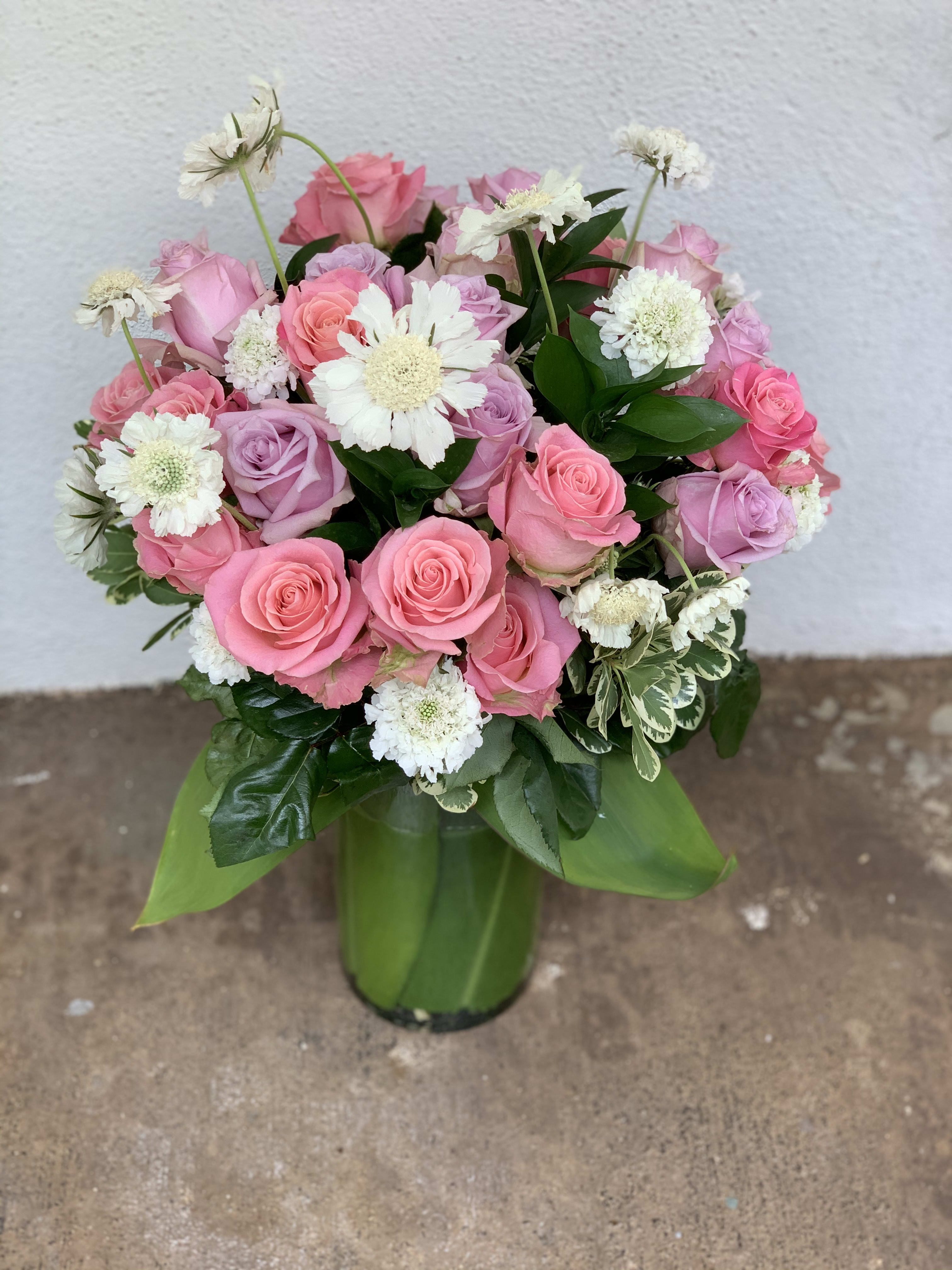 Pink and lavender roses arranged with white daisies in a green vase