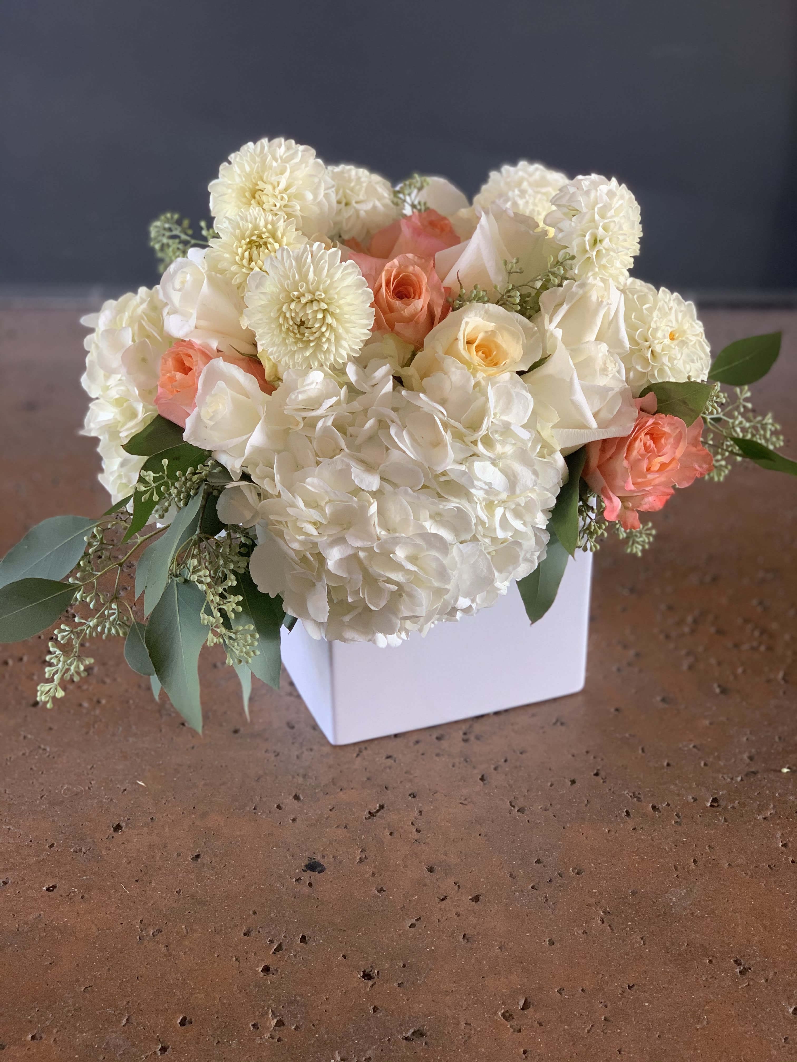 White and peach floral arrangement in a white square vase