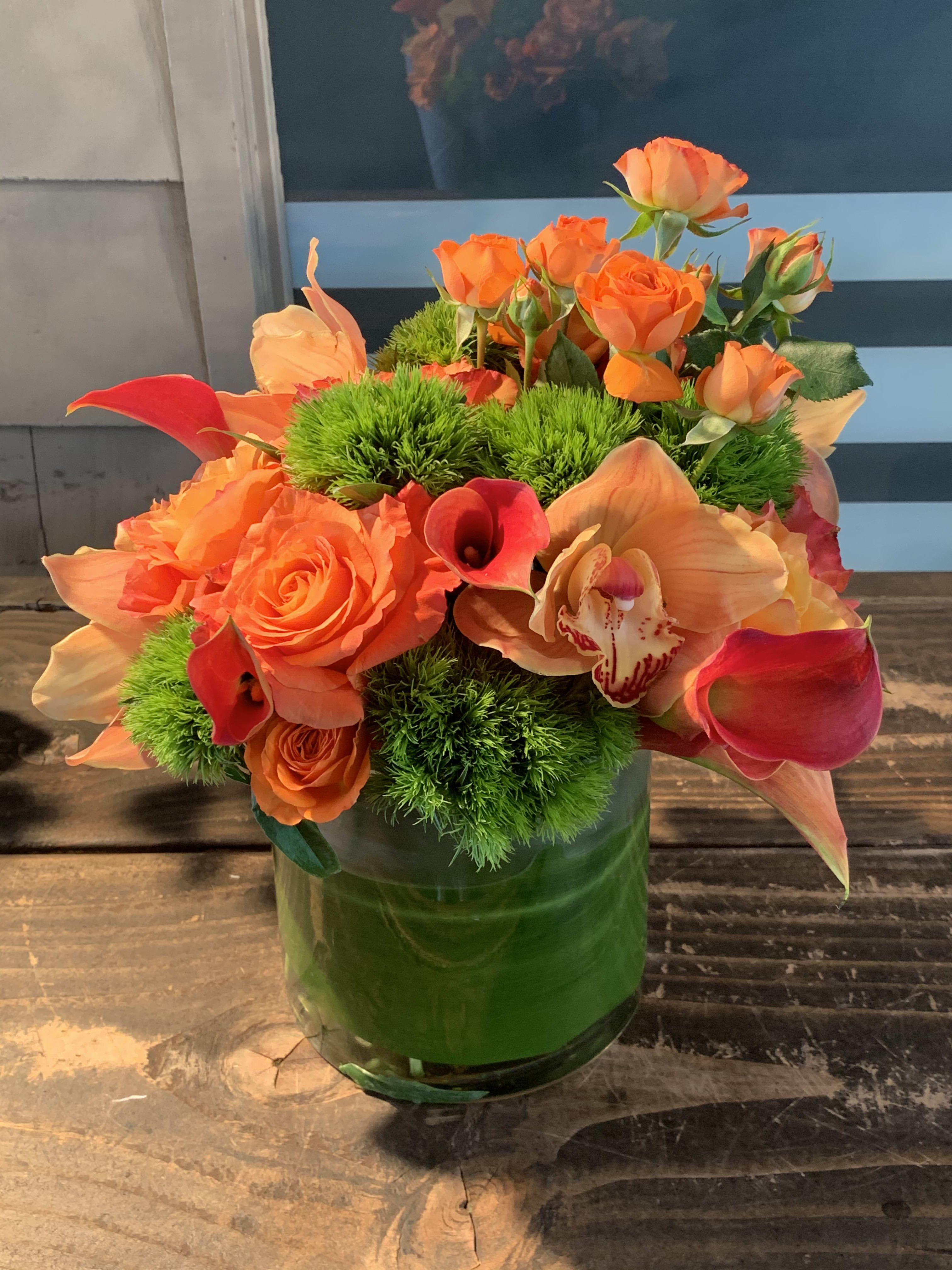 Orange roses and calla lilies in a green glass vase