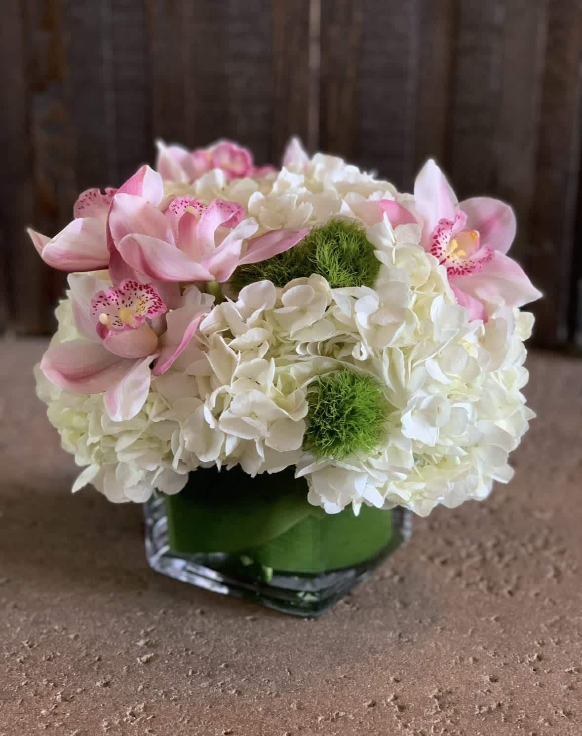 Pink orchids and white hydrangeas in a square glass vase