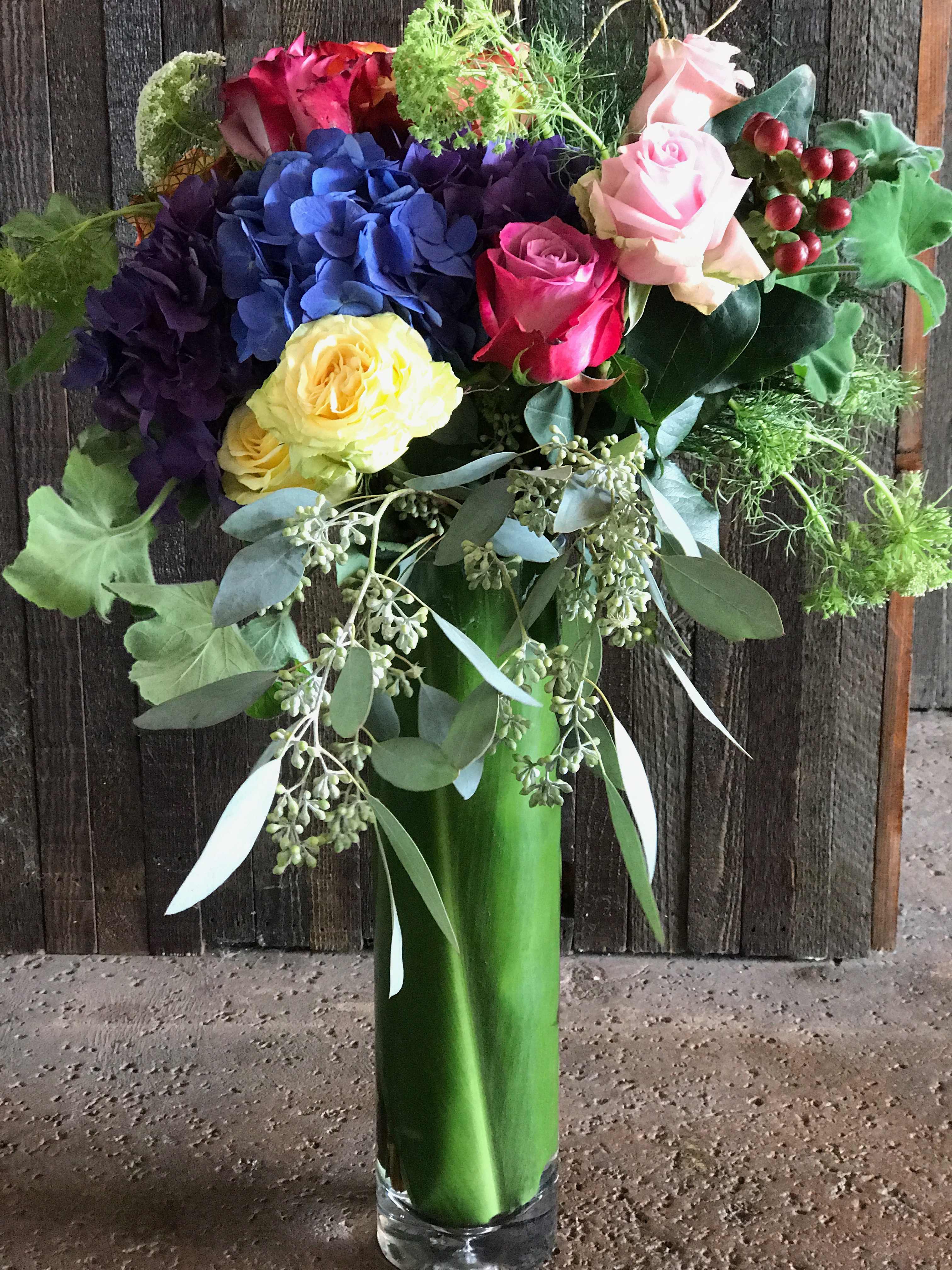Colorful bouquet of roses and hydrangeas in a tall glass vase