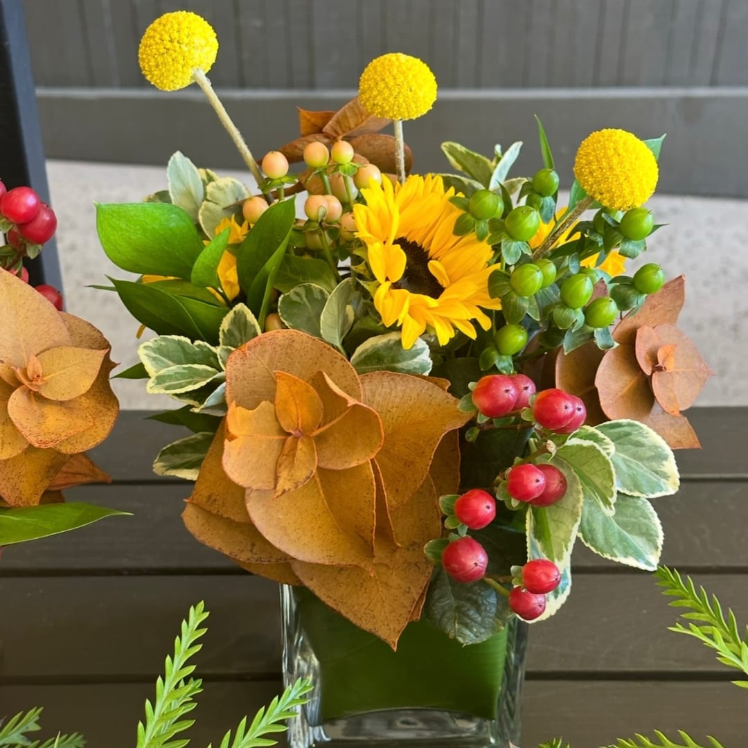 Yellow sunflower arrangement in a clear glass vase with autumn-colored accents