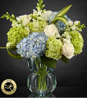 The FTD® Superior Sights™ Luxury Bouquet - Clusters of blue and green hydrangea give this floral arrangement a fresh focus, drawing the eye with pops of white roses and snapdragons perfectly placed with an artist's eye to create an unforgettable moment upon delivery. Notice how the flax leaves are placed within the arrangement to give it all a sense of movement and grace, taking the design aesthetic to a new level of sophistication. The subtle light blue color of the vase helps to bring forth the blues and greens within the bouquet, making this both a warm and airy design that will help you send a gift that truly speaks from your heart. IMPRESSIVE bouquet includes 13 stems with vase. Approx. 19"H x 14"W. STUNNING bouquet includes 22 stems. Approx. 21"H x 16"W.  Your purchase includes a complimentary personalized gift message.