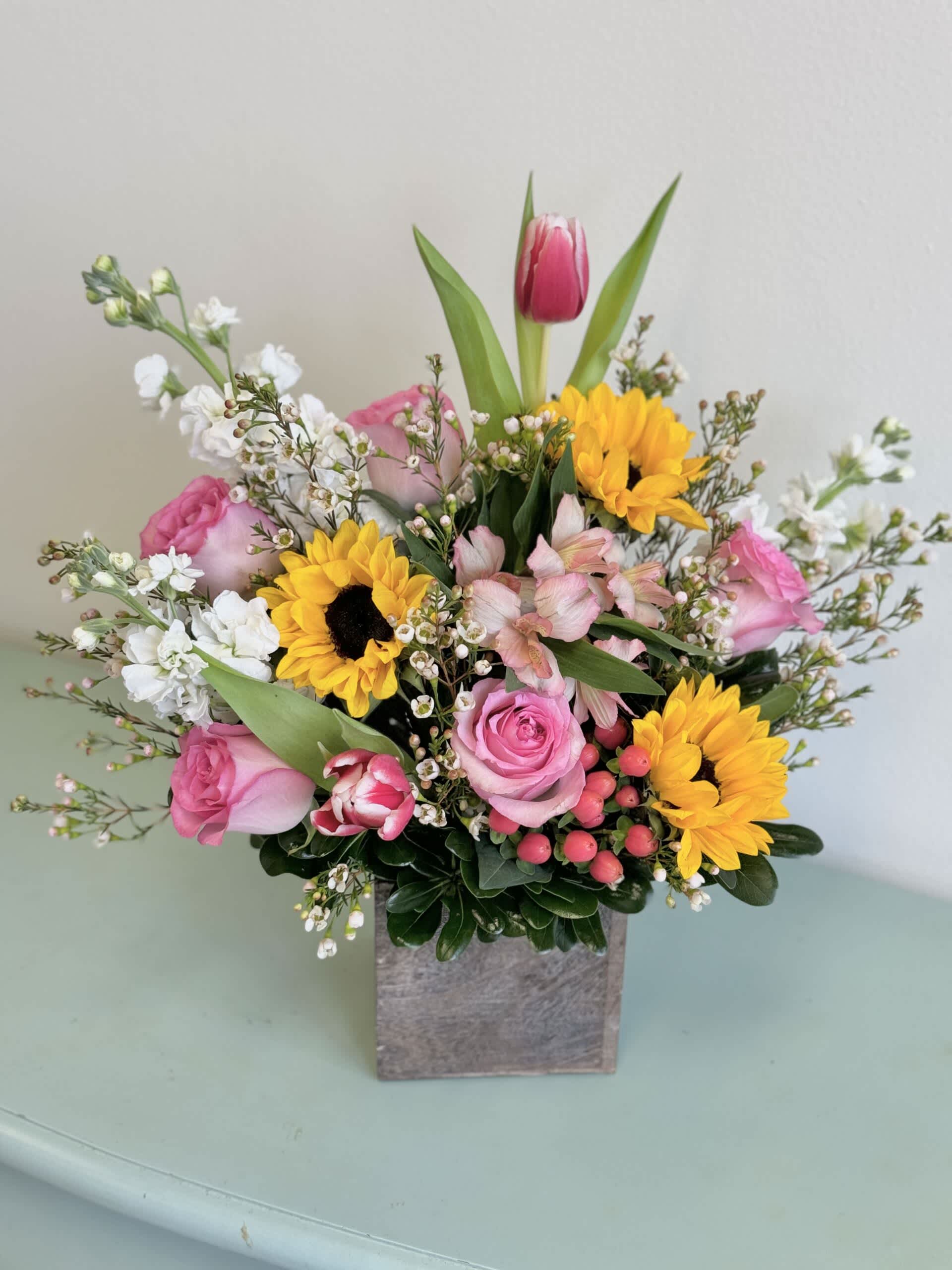 Mixed bouquet with pink roses, sunflowers, and white filler flowers in a square vase