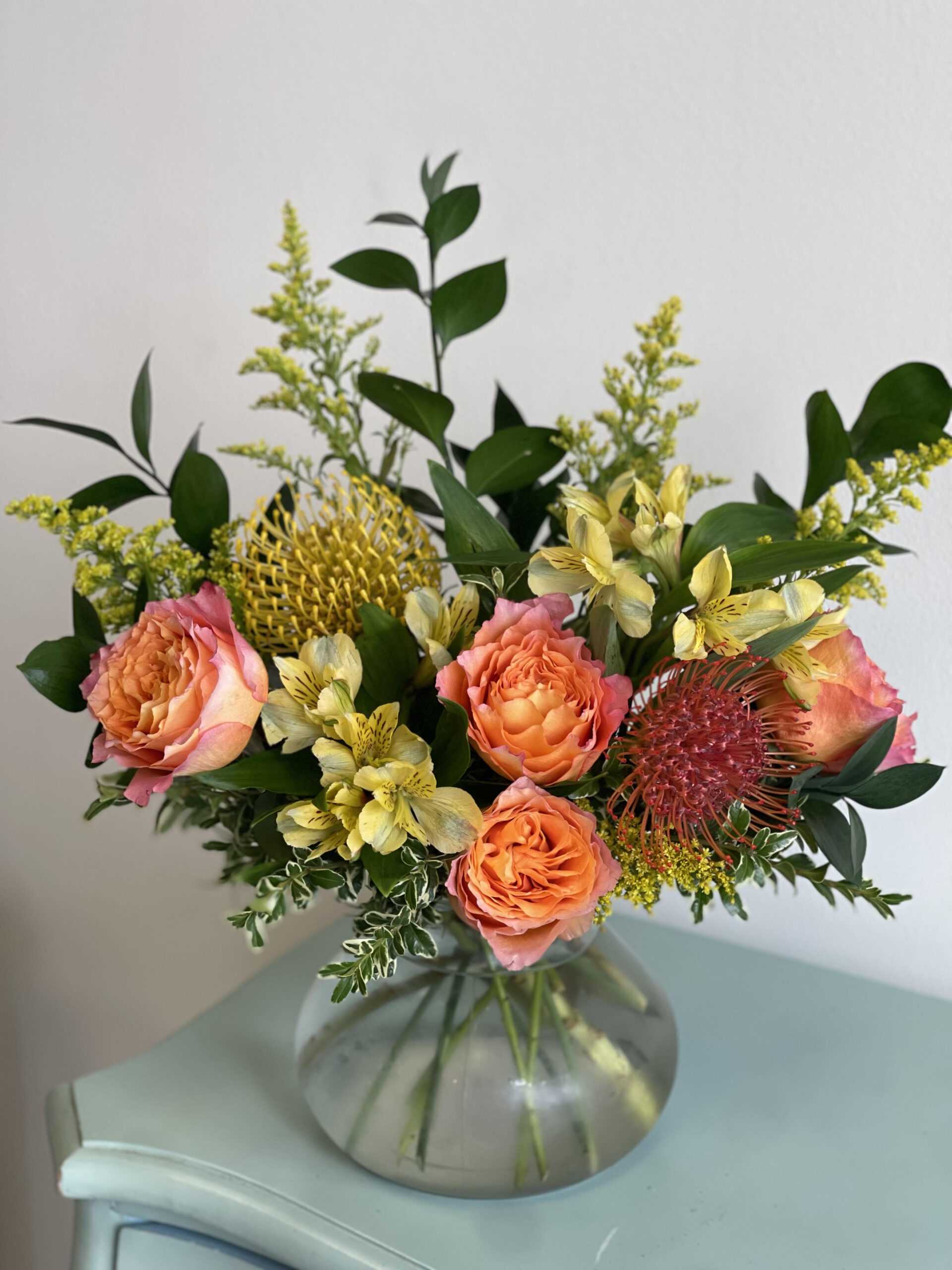 Bouquet of peach roses and yellow flowers in a round glass vase