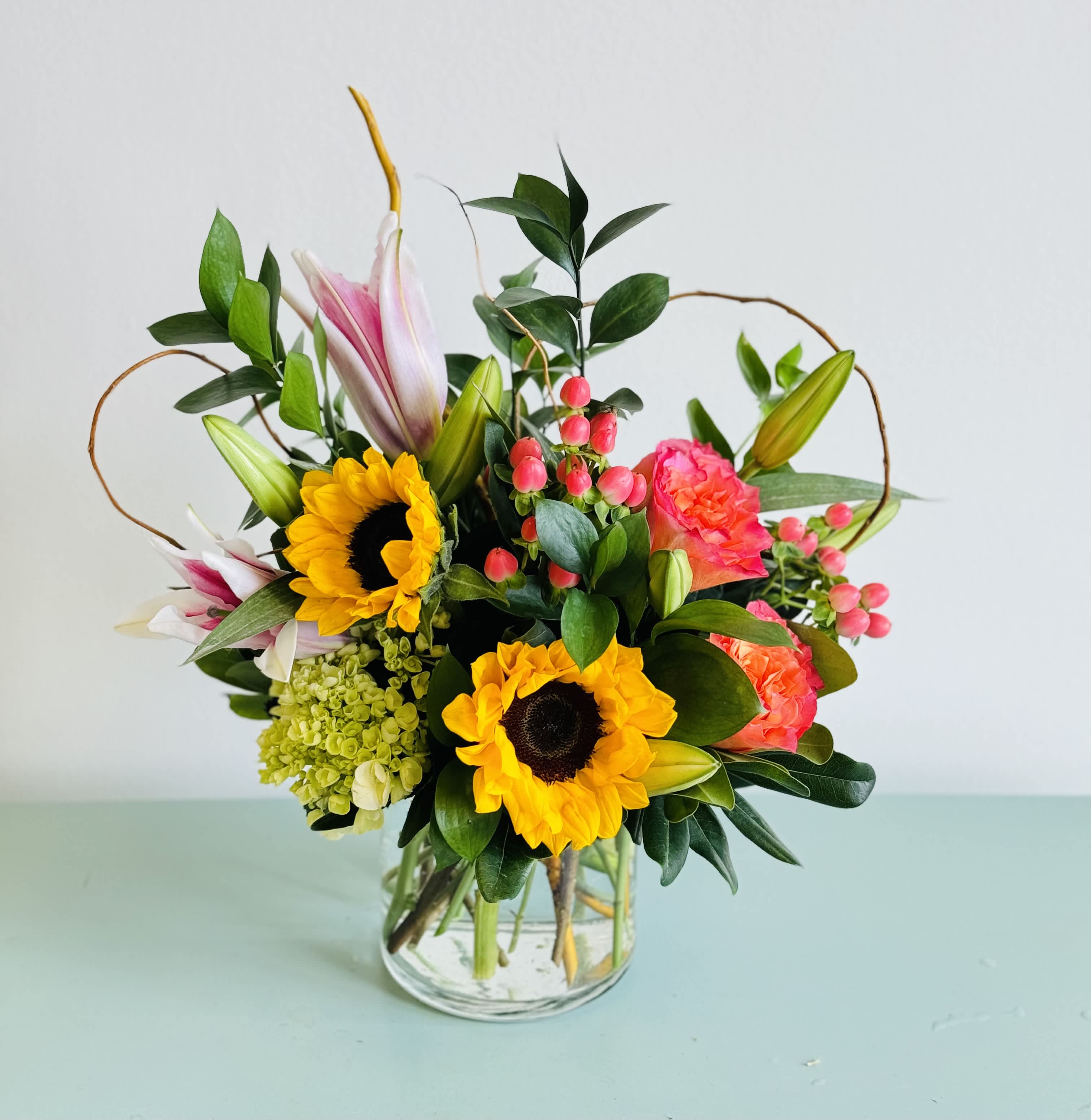 Mixed bouquet with sunflowers, lilies, and pink blooms in a glass vase