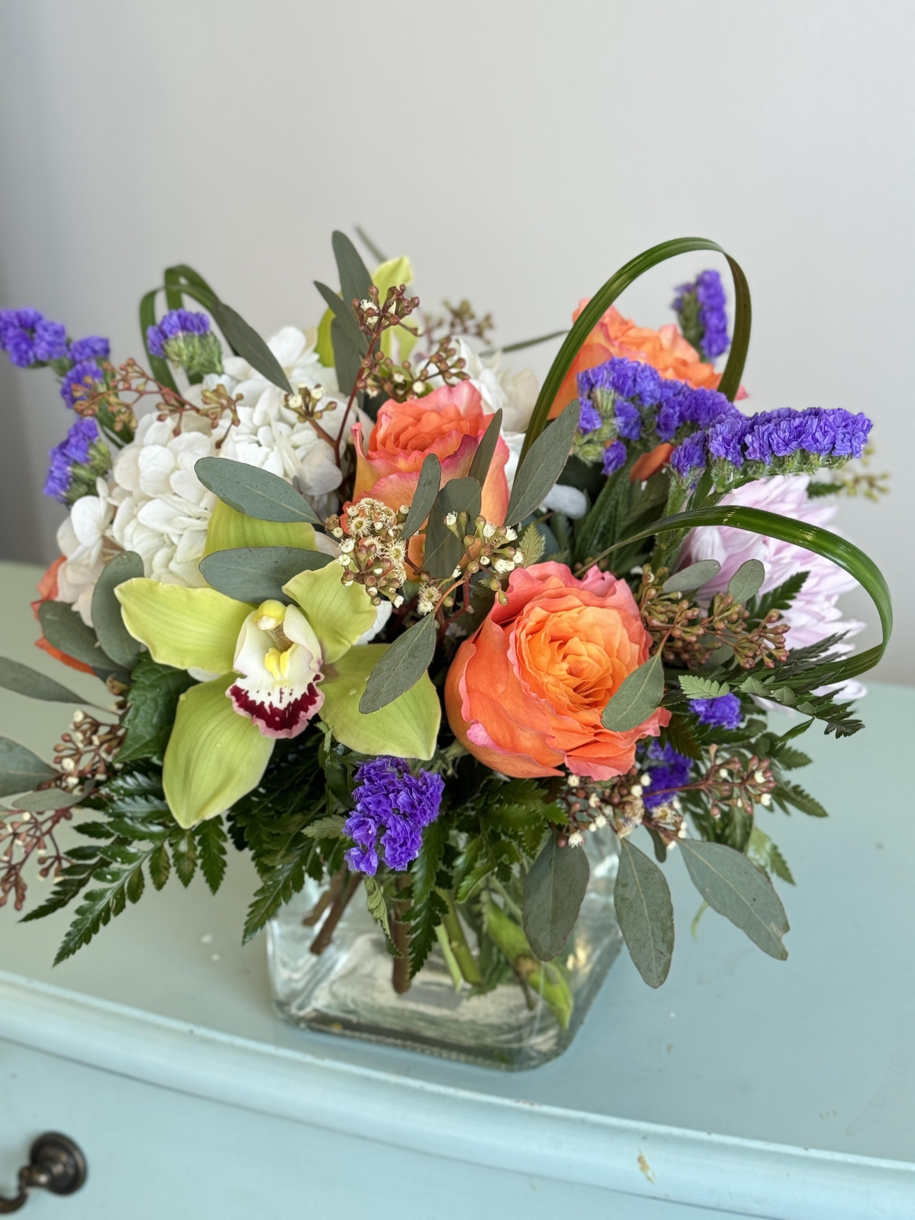 Mixed bouquet in a square glass vase with orange roses and green orchids