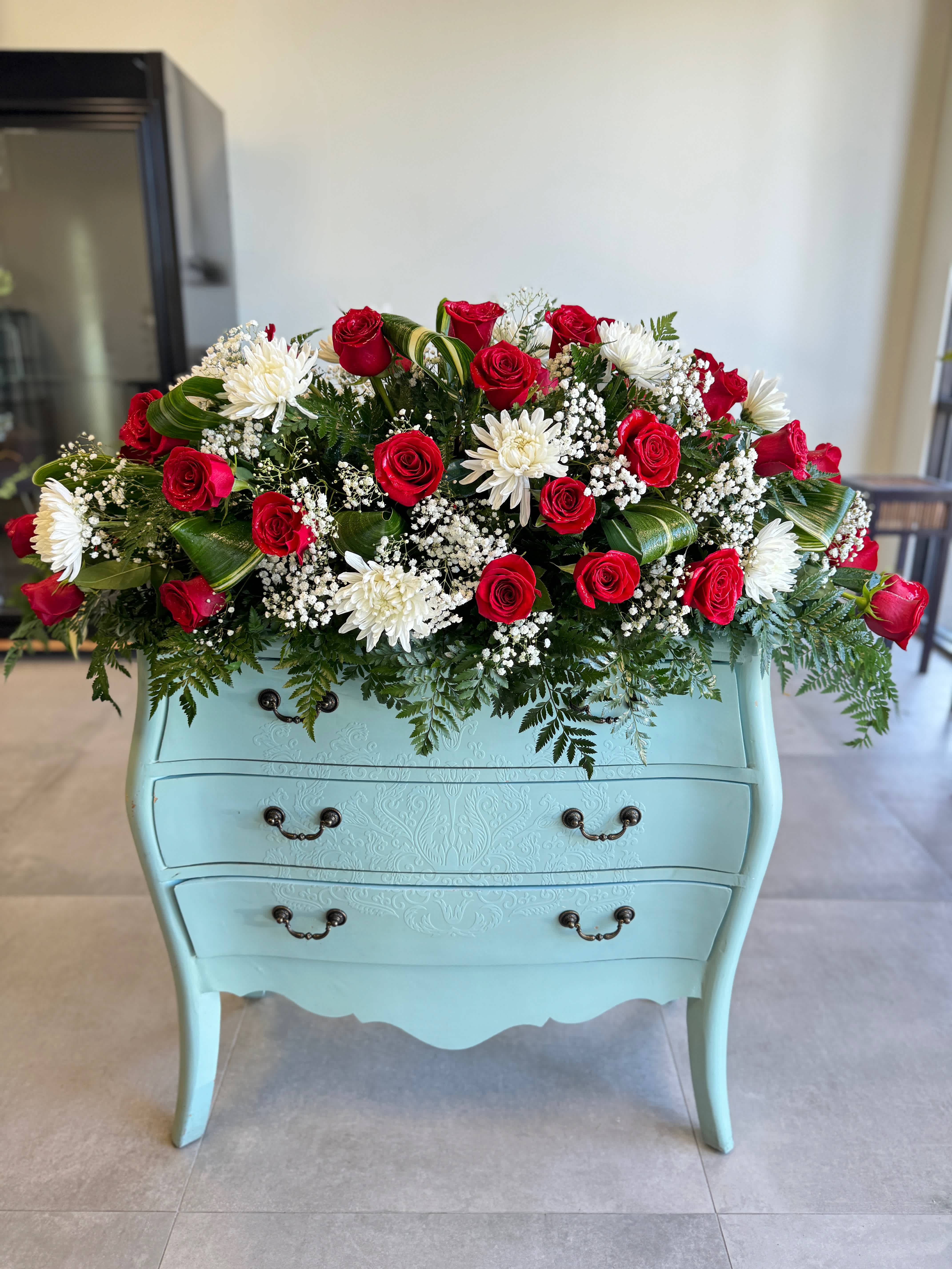 Red roses and white daisies arranged on a light blue dresser