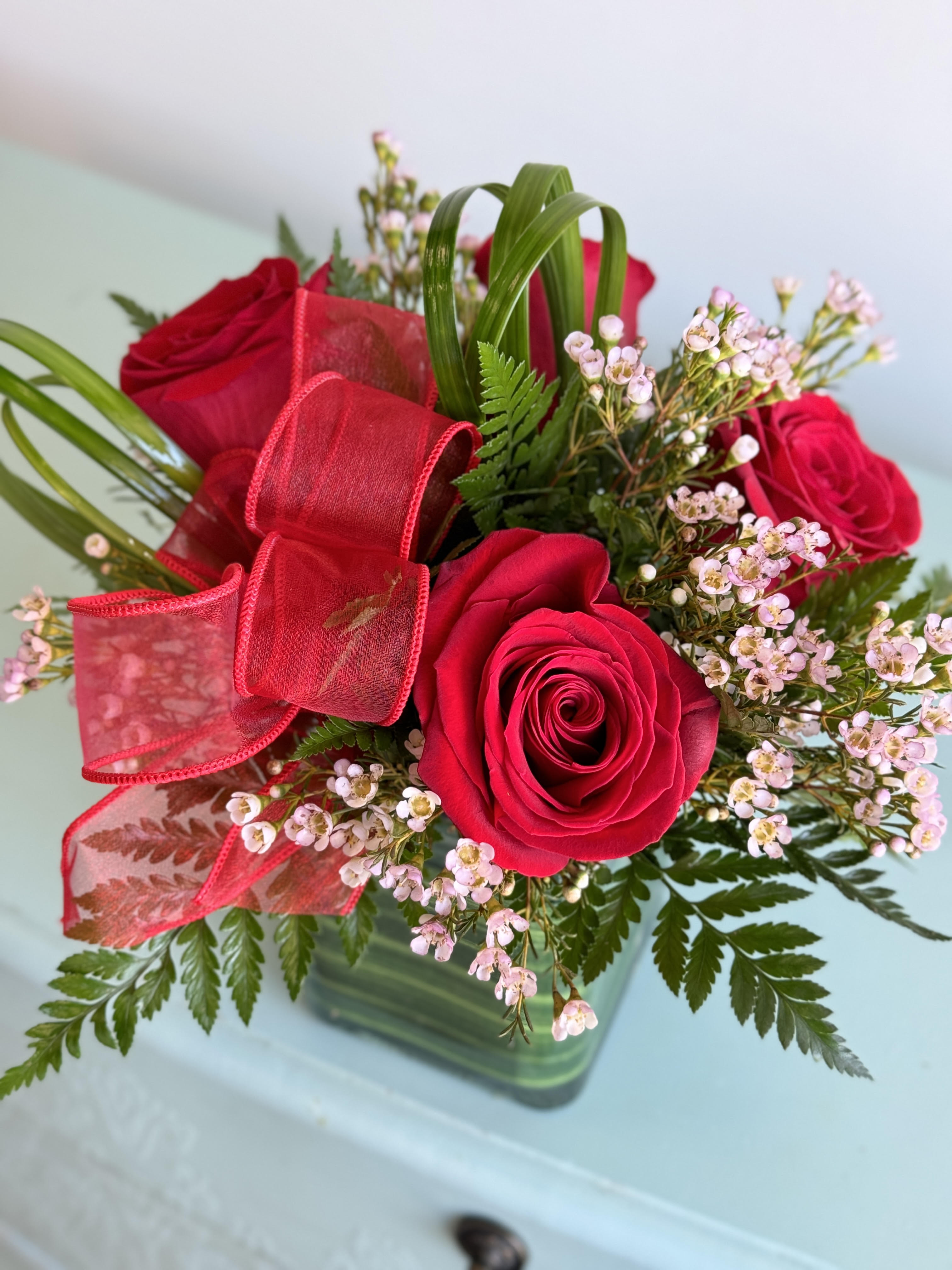Red roses with pink filler flowers and a red ribbon in a glass vase
