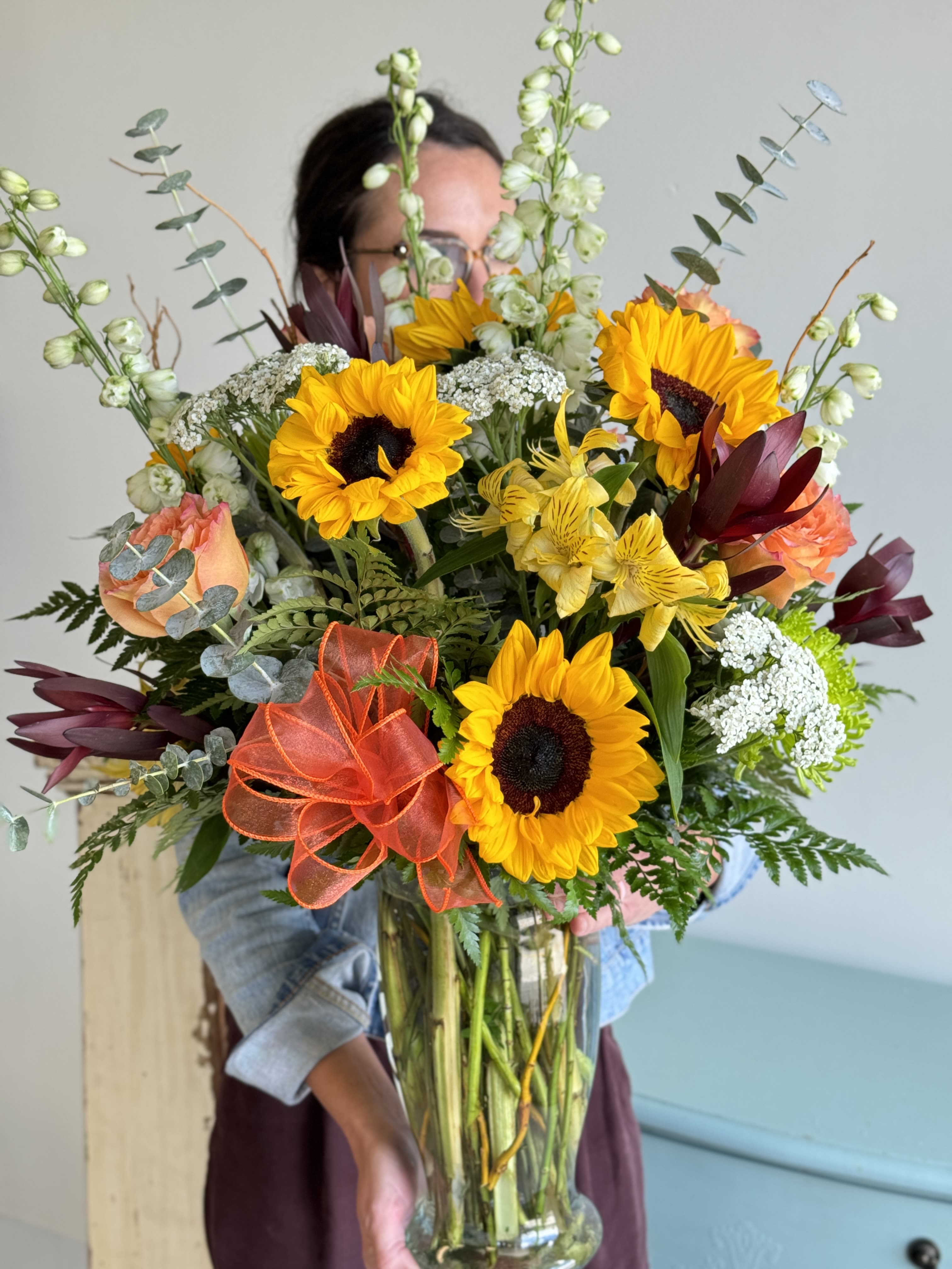 Large mixed bouquet with sunflowers, roses, and yellow alstroemeria in a glass vase.