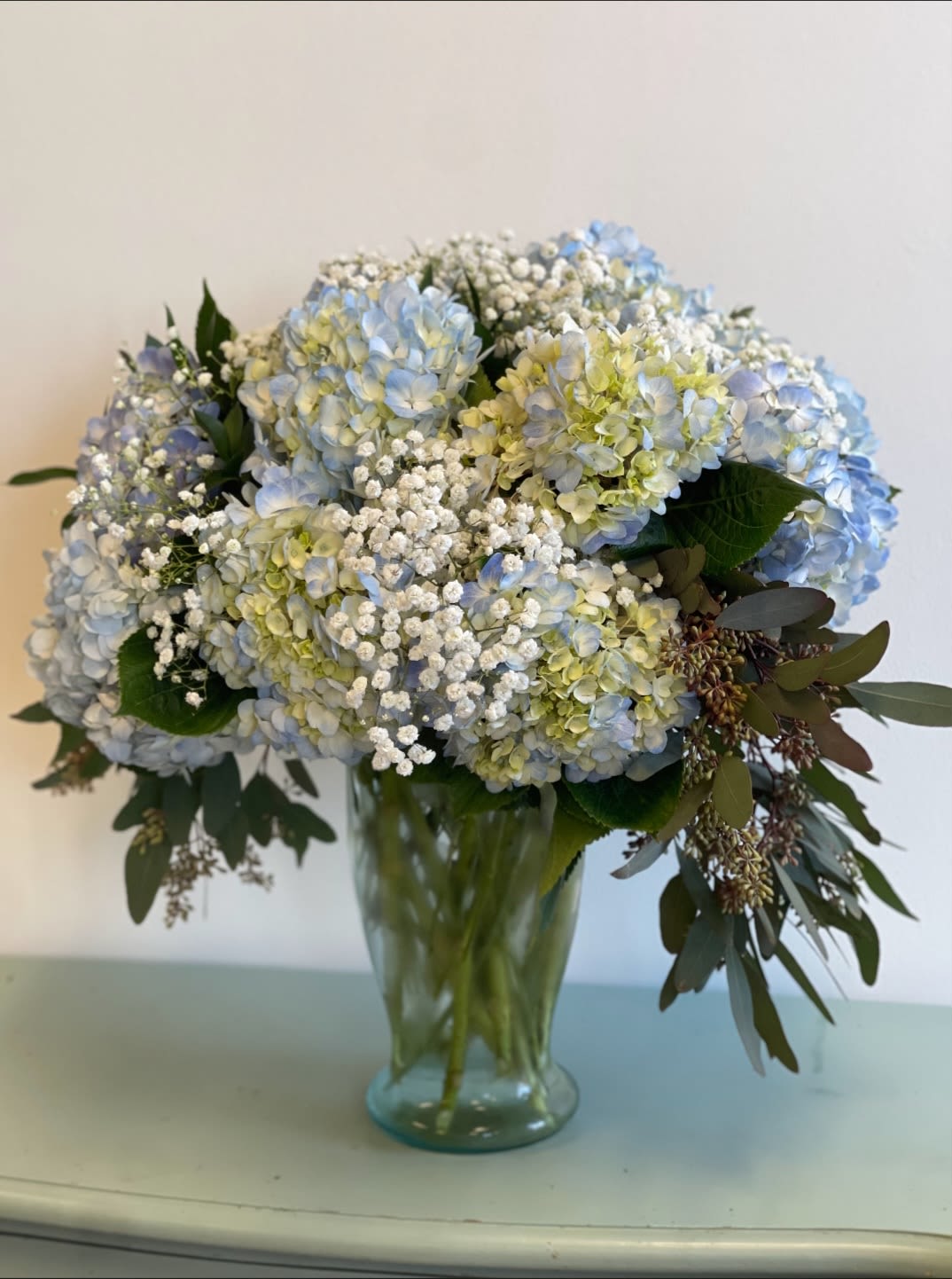 Blue hydrangea bouquet in a glass vase with white filler flowers