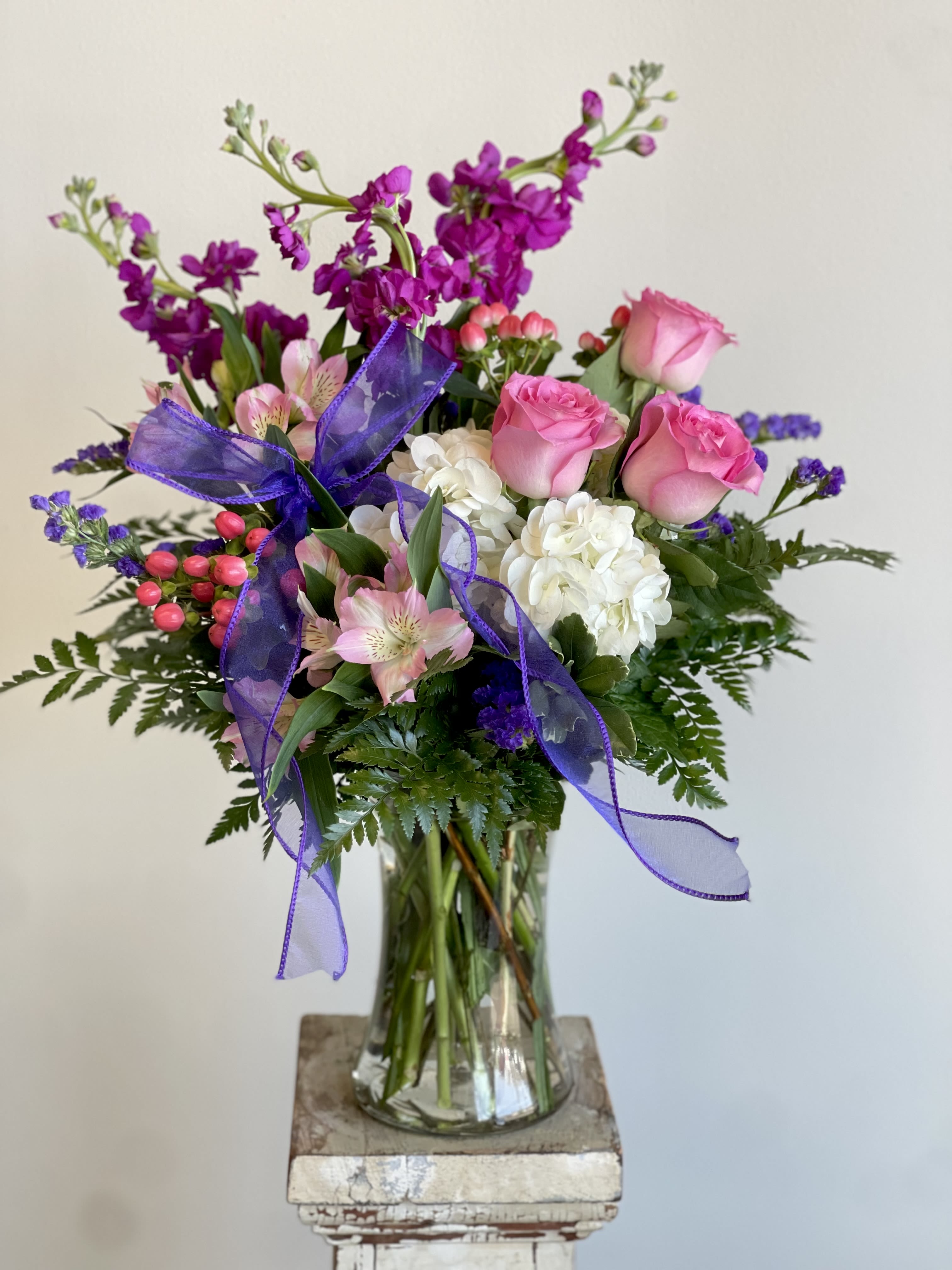 Pink roses and white hydrangeas in a glass vase with purple ribbon