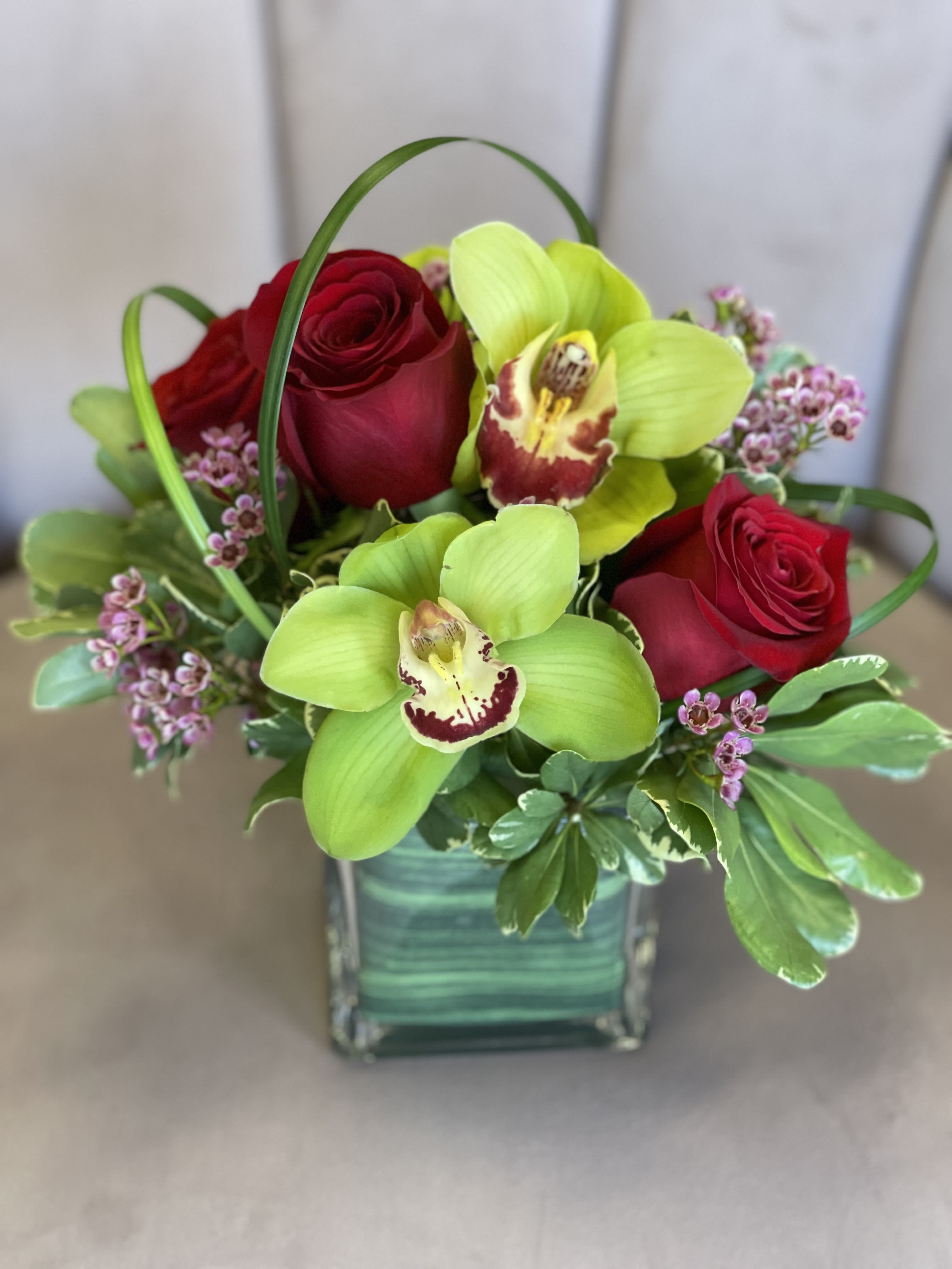 Red roses and green orchids arranged in a square glass vase