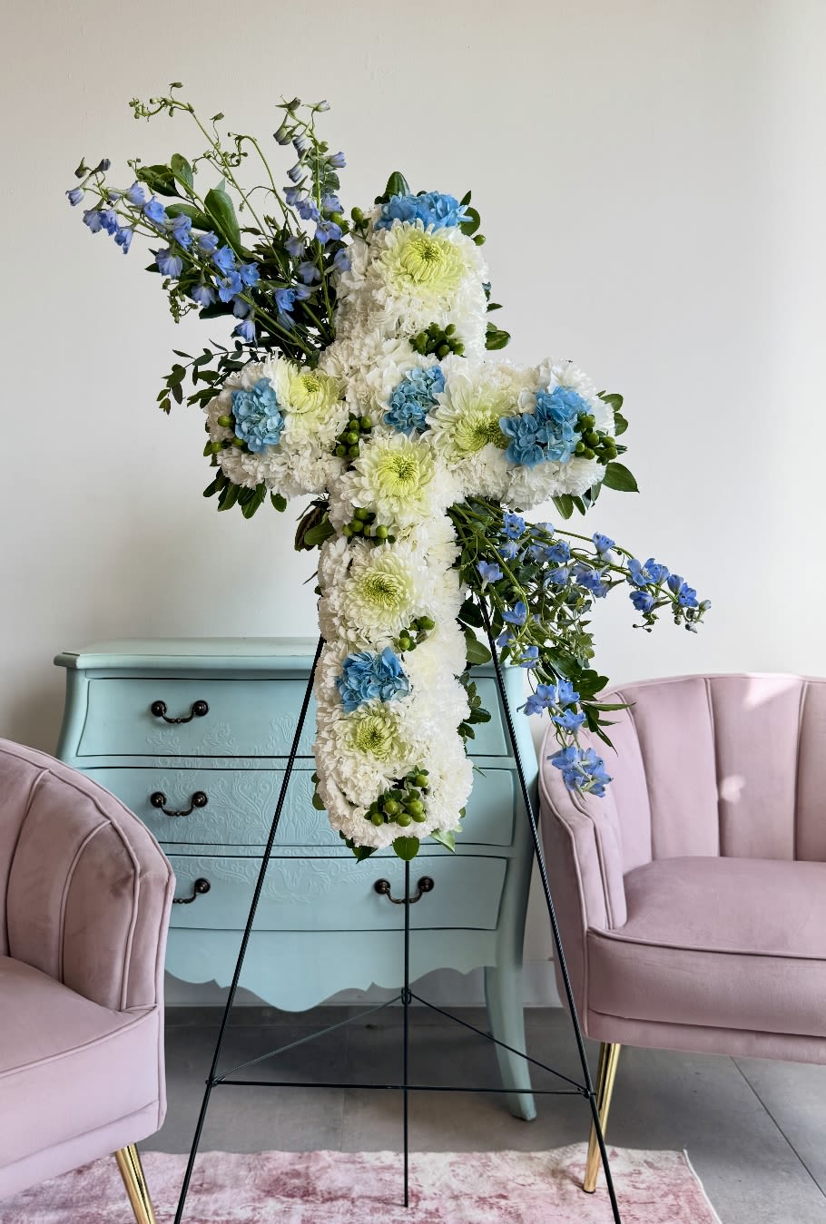 Large floral cross on a stand with white, blue, and green flowers