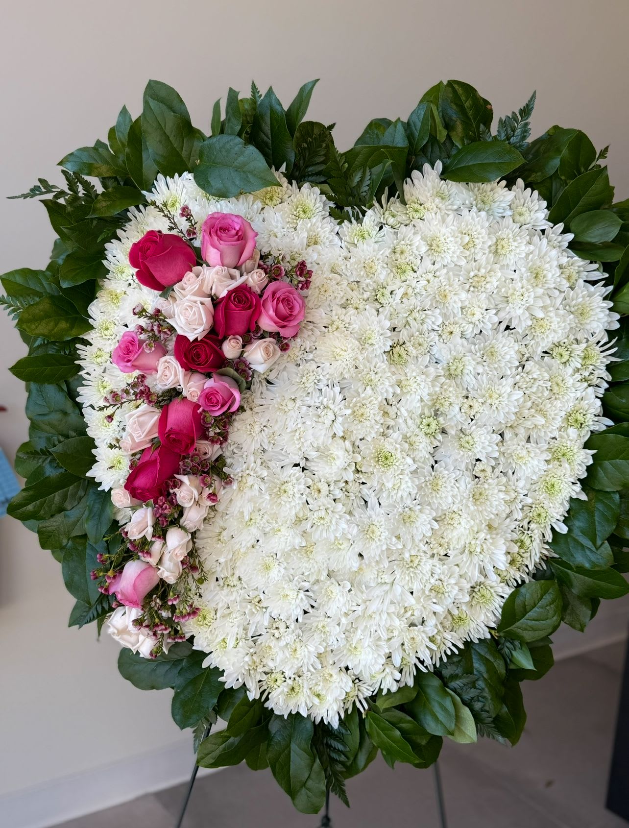 Heart-shaped white chrysanthemum wreath with pink roses and a green leaf border