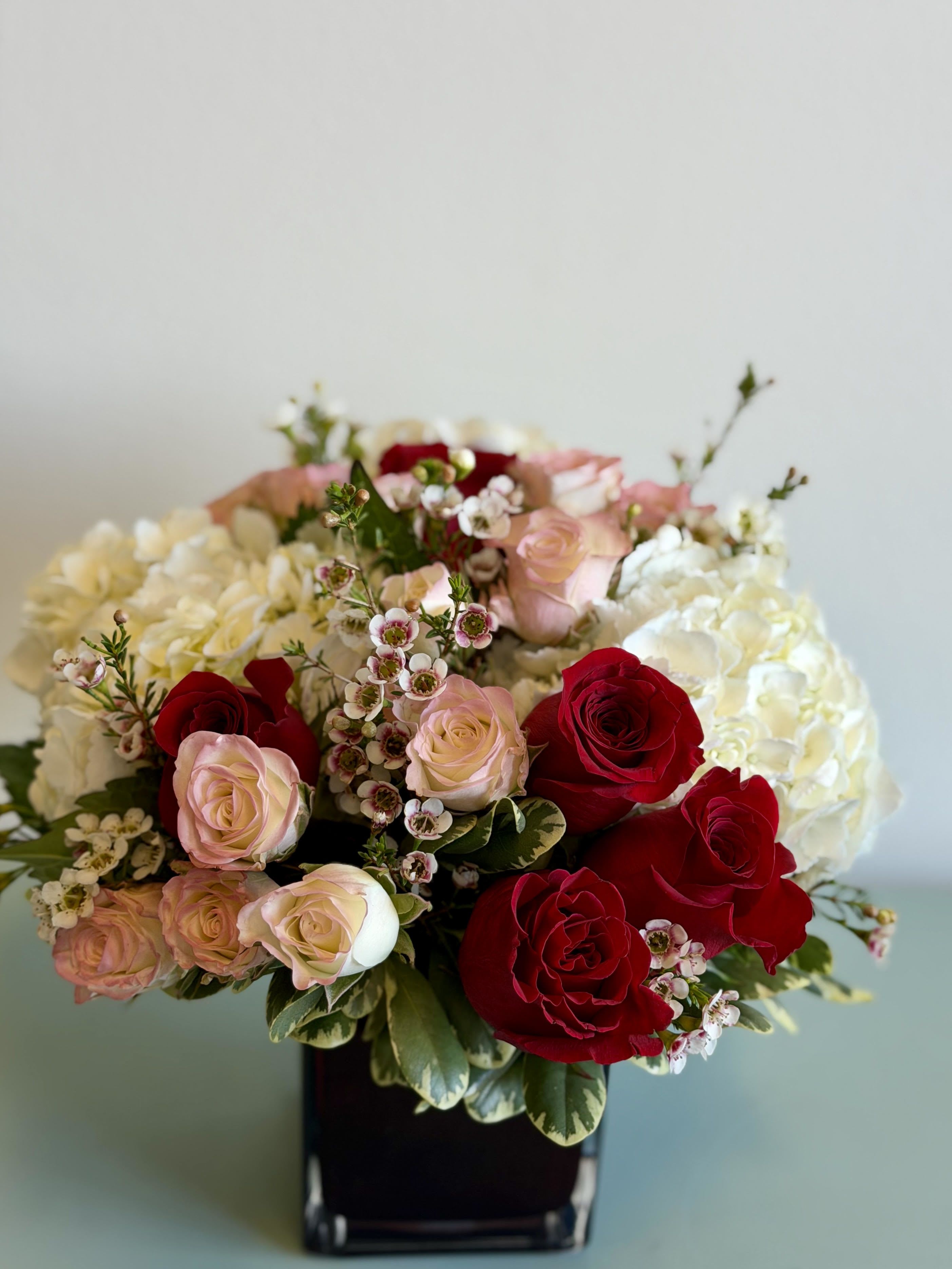 Bouquet of red and blush roses with white hydrangeas in a black vase