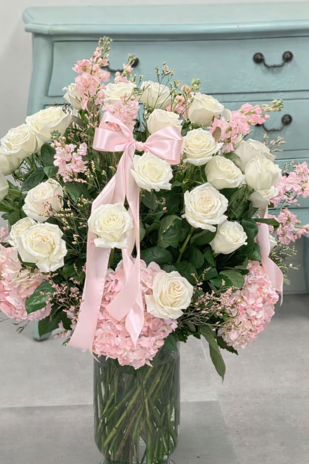 White roses and pink hydrangeas in a glass vase with a pink ribbon