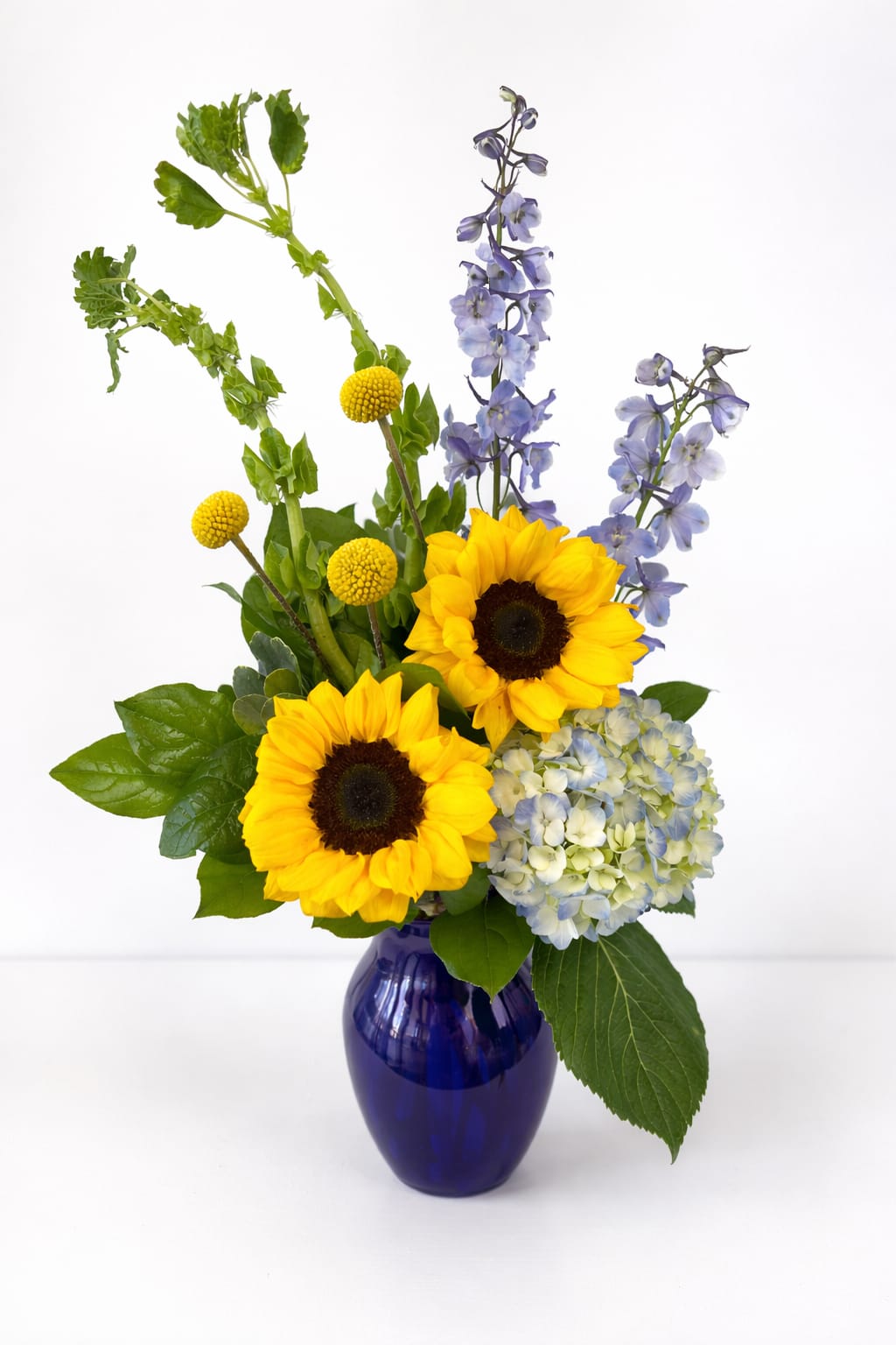Sunny bouquet with sunflowers, blue hydrangea, delphinium and Bells of Ireland in a cobalt glass vase