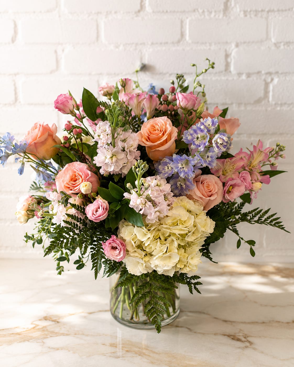 Mixed bouquet of pink, peach, lavender, and white flowers in a glass vase