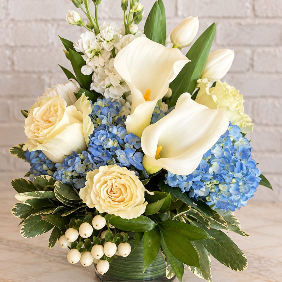 White calla lilies, cream roses, and blue hydrangeas in a green vase
