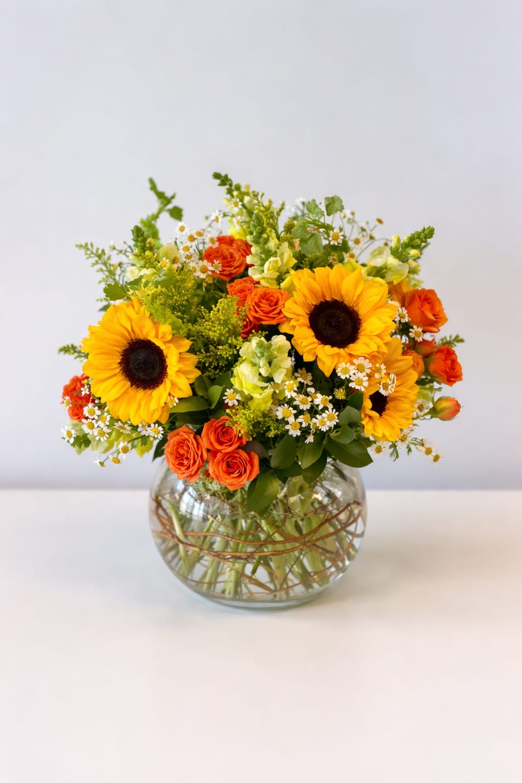 Sunflower and orange rose arrangement in a round glass vase
