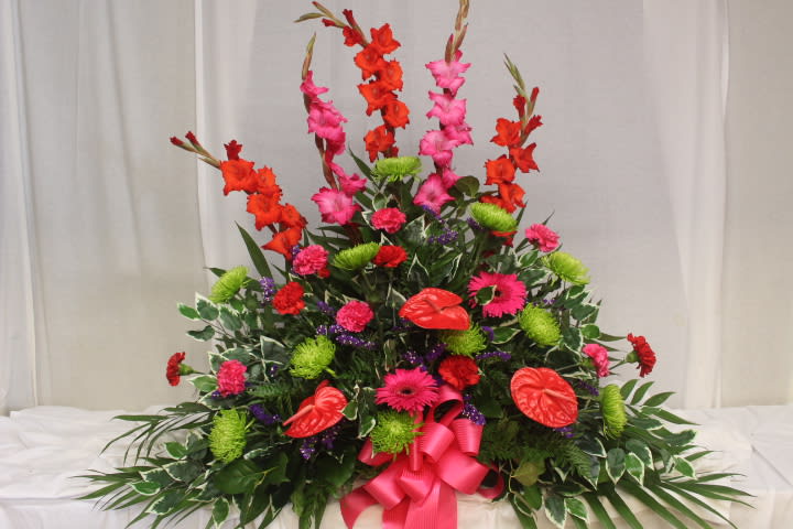 Tall floral spray with red and pink blooms and a bright pink ribbon