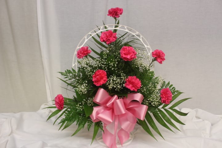 Pink carnation arrangement with a large pink bow in a white basket