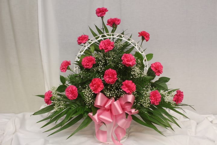 Pink carnations in a white basket with a pink ribbon