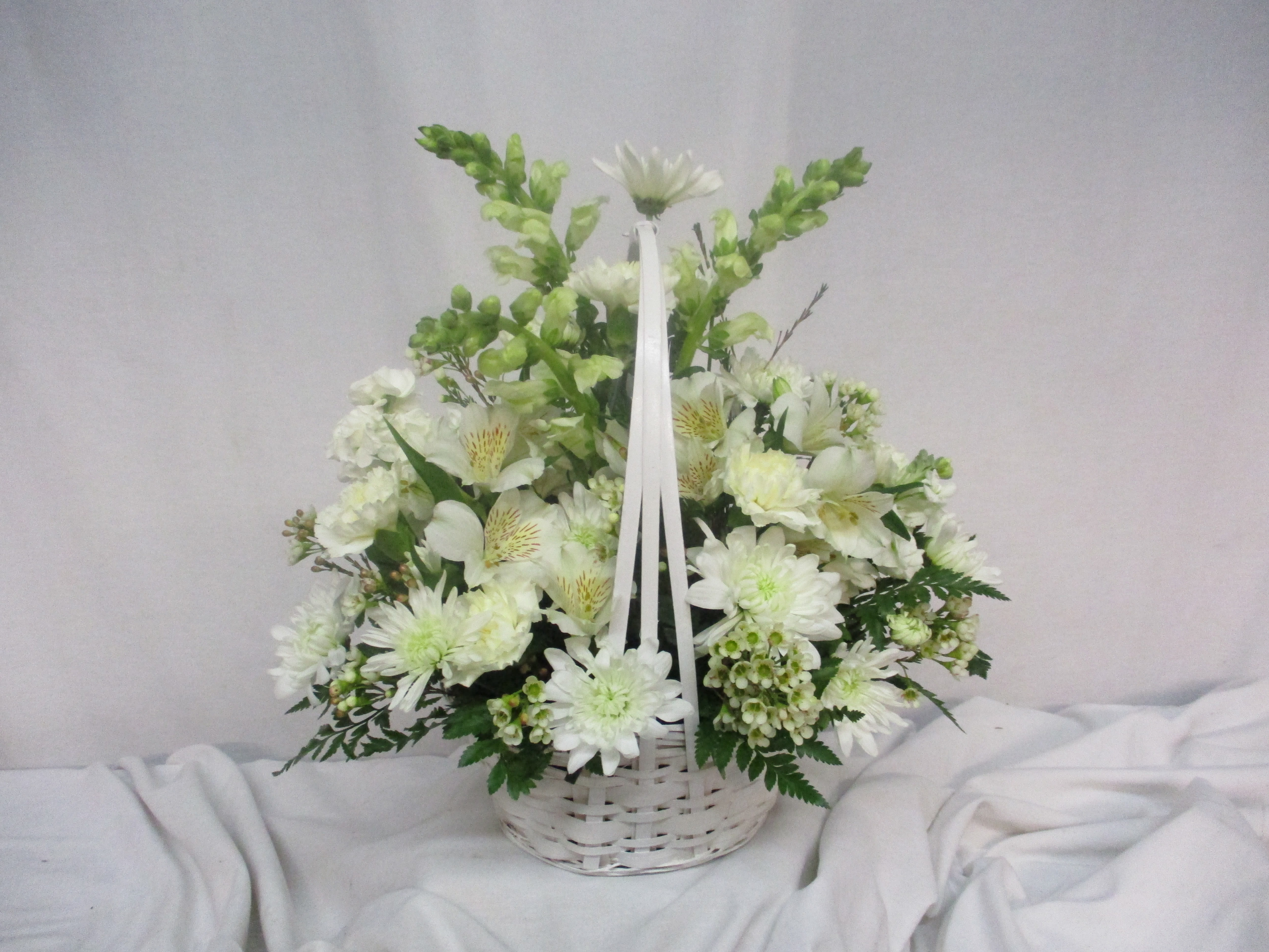 White floral arrangement in a white wicker basket with ribbon handles