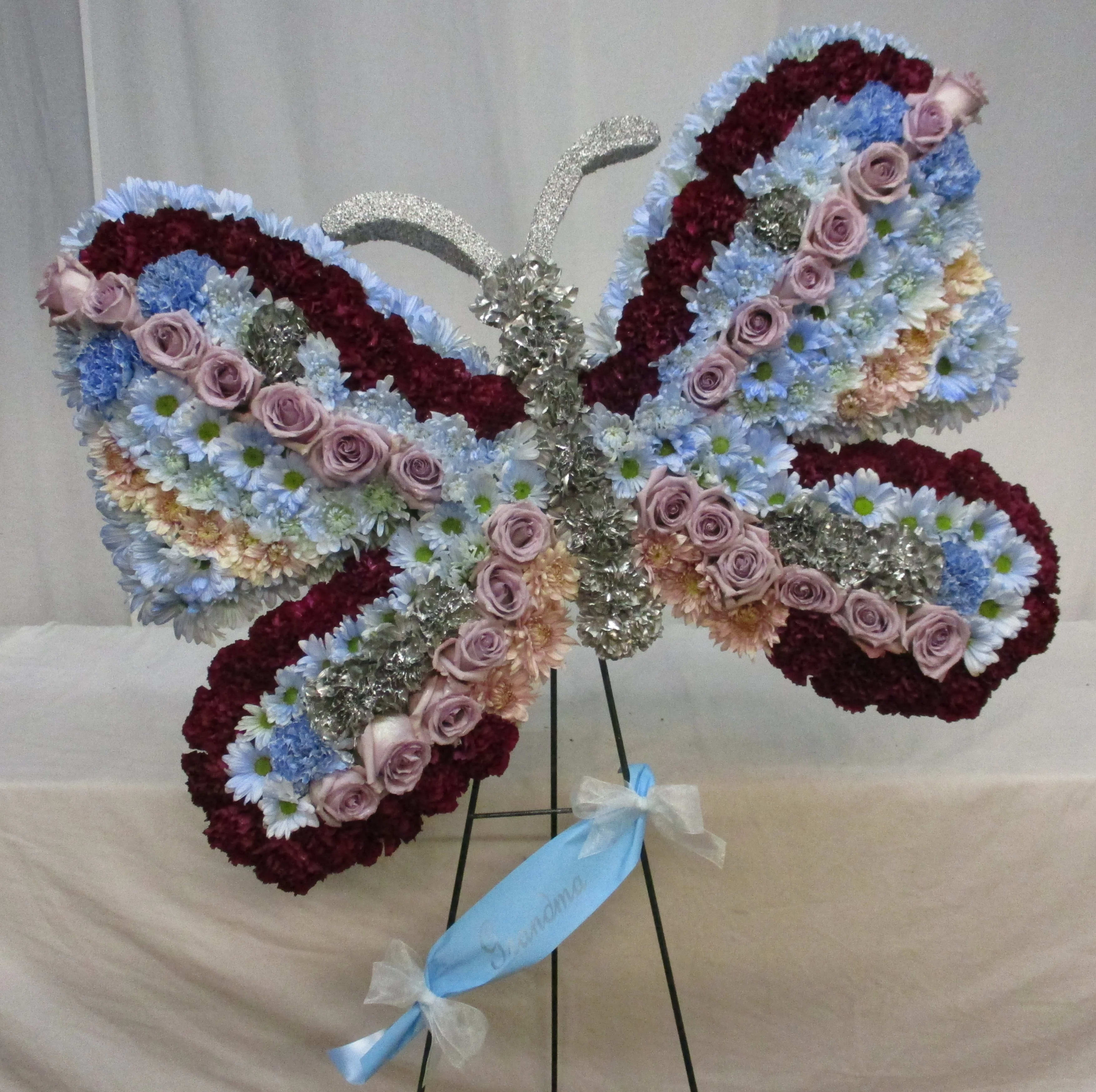 Butterfly-shaped floral standing spray with pink roses and blue daisies