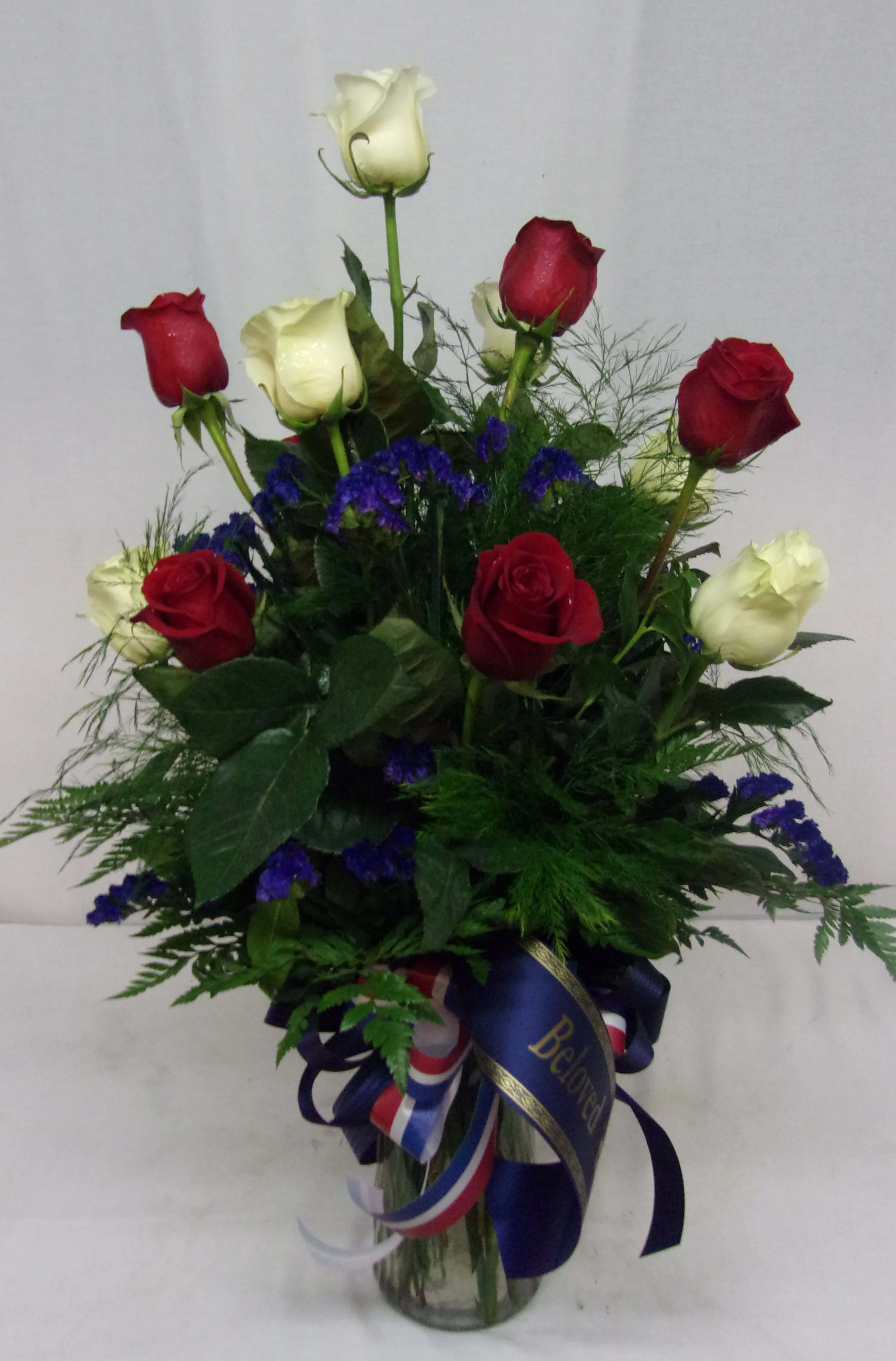 Red and white roses arranged in a glass vase with blue filler flowers.