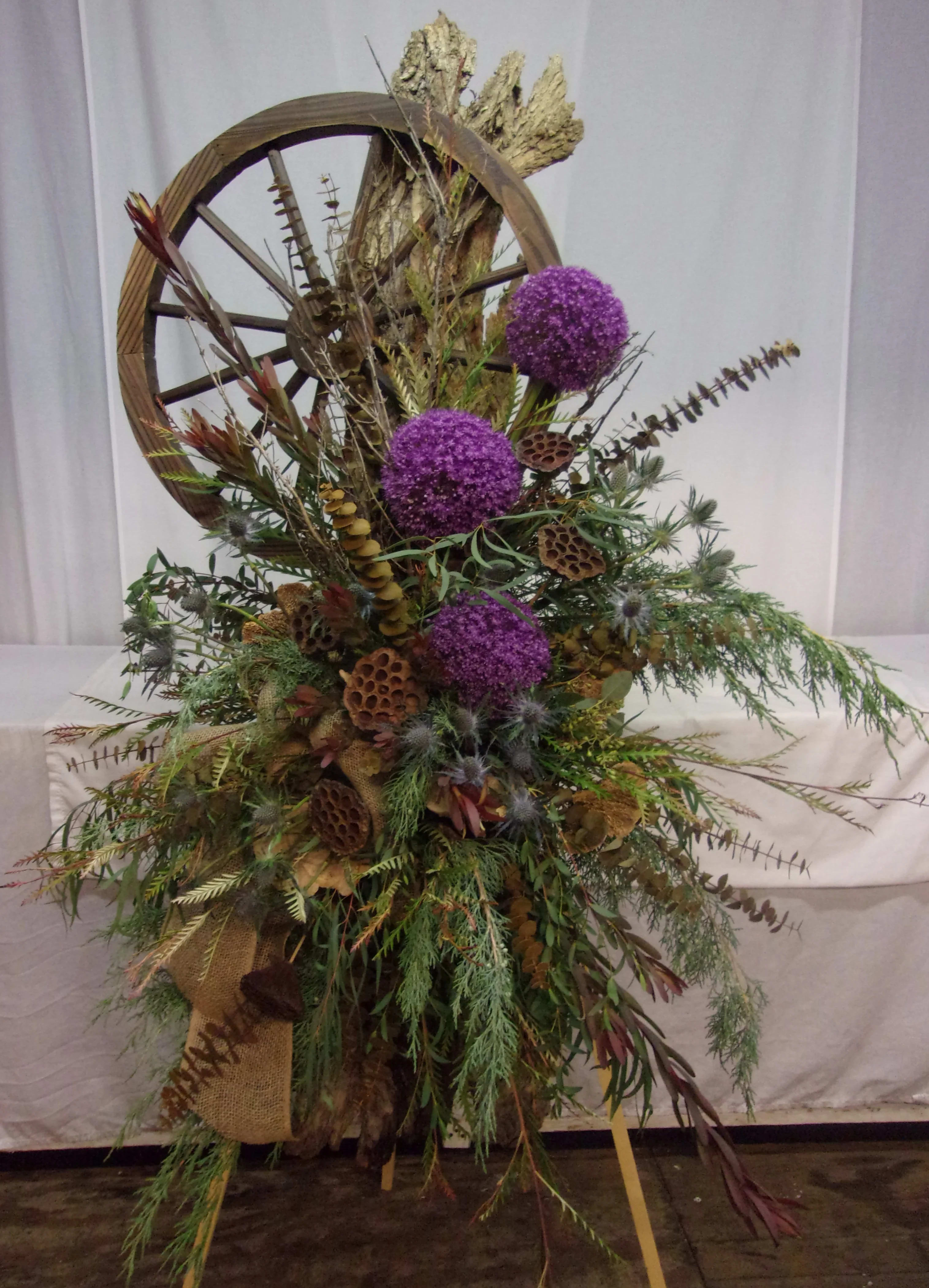 Tall rustic arrangement with purple globe flowers and dried botanicals on a wagon wheel frame
