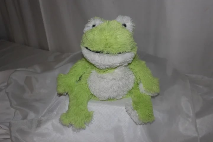 Green and white plush frog toy sitting on a bed