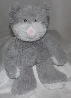 Gray plush teddy bear with a pink nose sitting on a bed