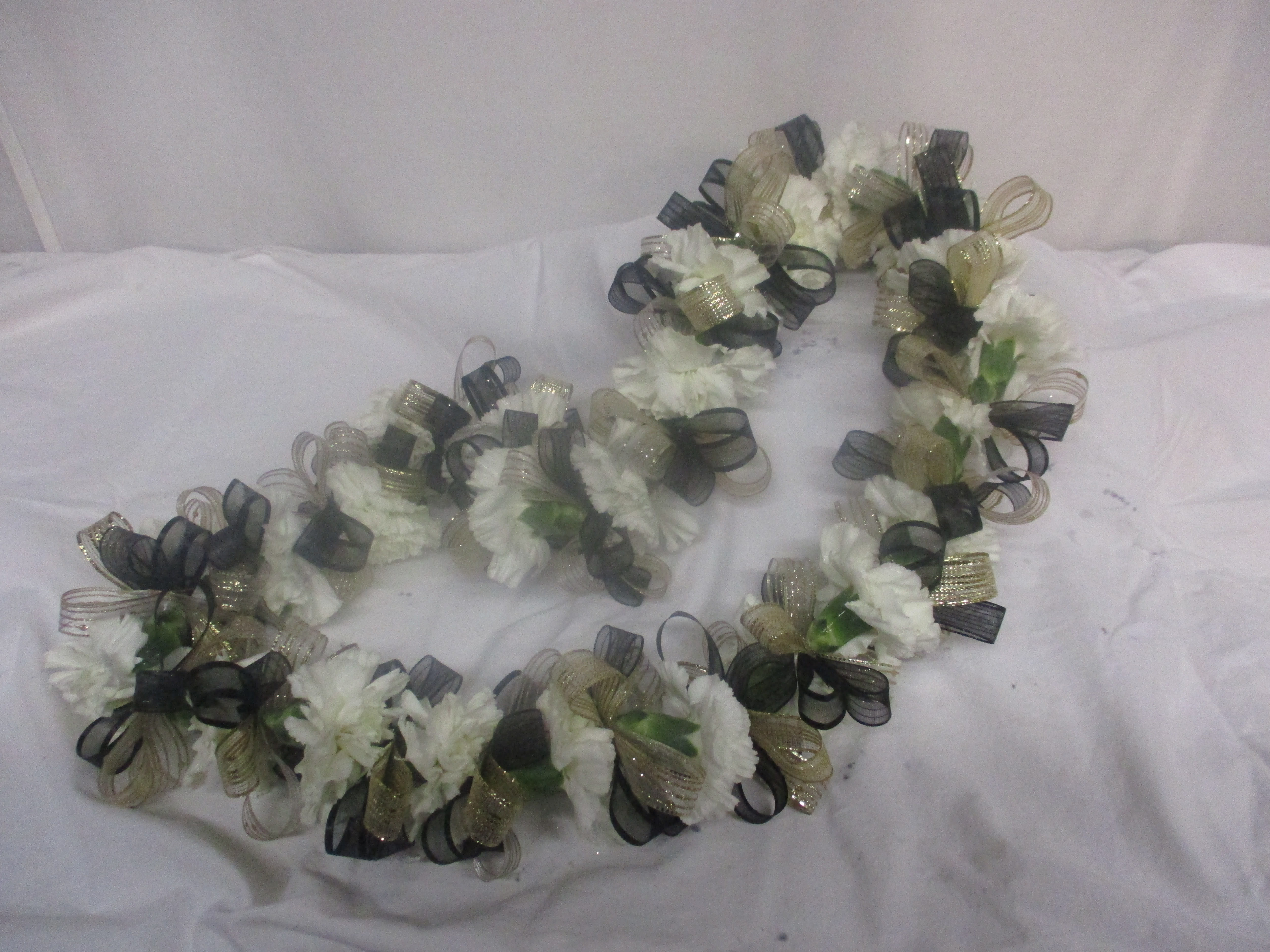 White floral lei with black and gold ribbon loops