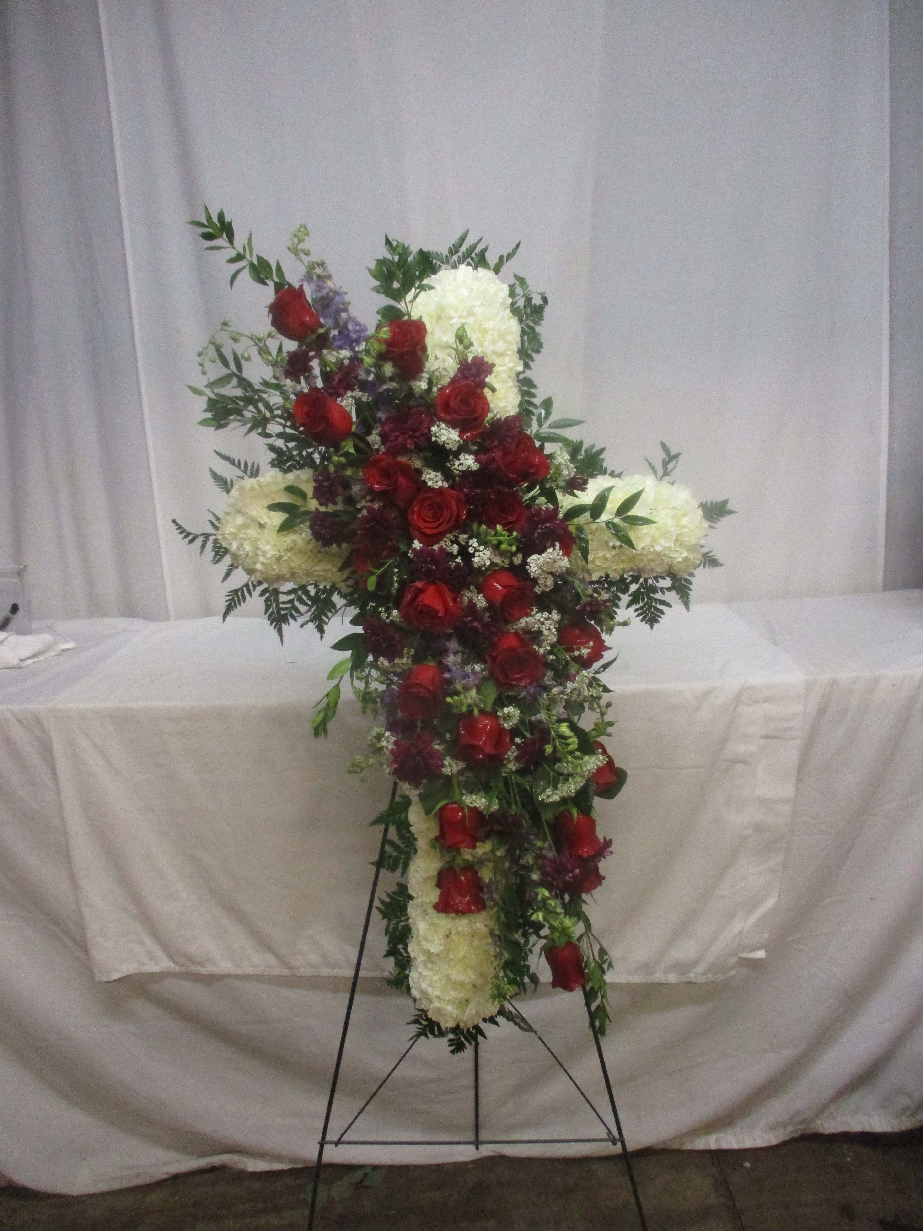 Cross-shaped floral arrangement with red roses and white blooms on a stand