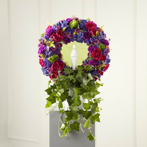 Circular floral wreath with purple, pink, and blue flowers above trailing ivy