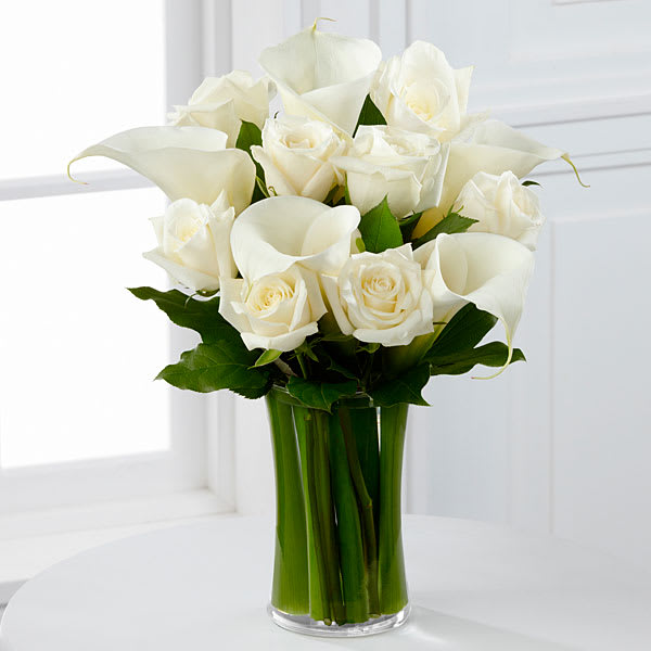 White roses and calla lilies arranged in a clear glass vase.