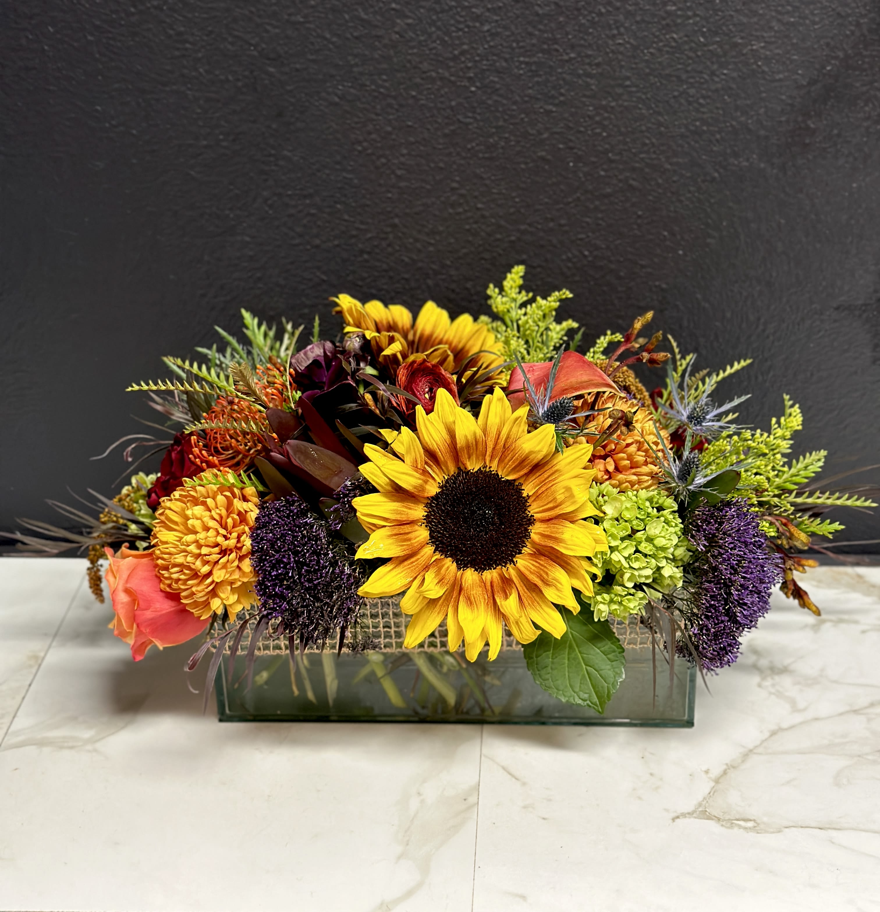 Mixed bouquet with sunflowers, roses, and chrysanthemums in a rectangular glass vase