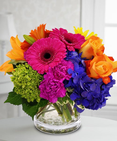 Colorful bouquet of gerbera daisies, roses, and hydrangeas in a glass vase