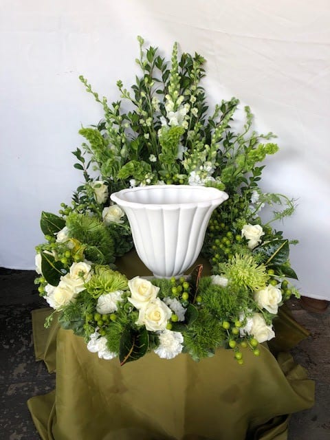 White urn surrounded by green and white floral arrangement