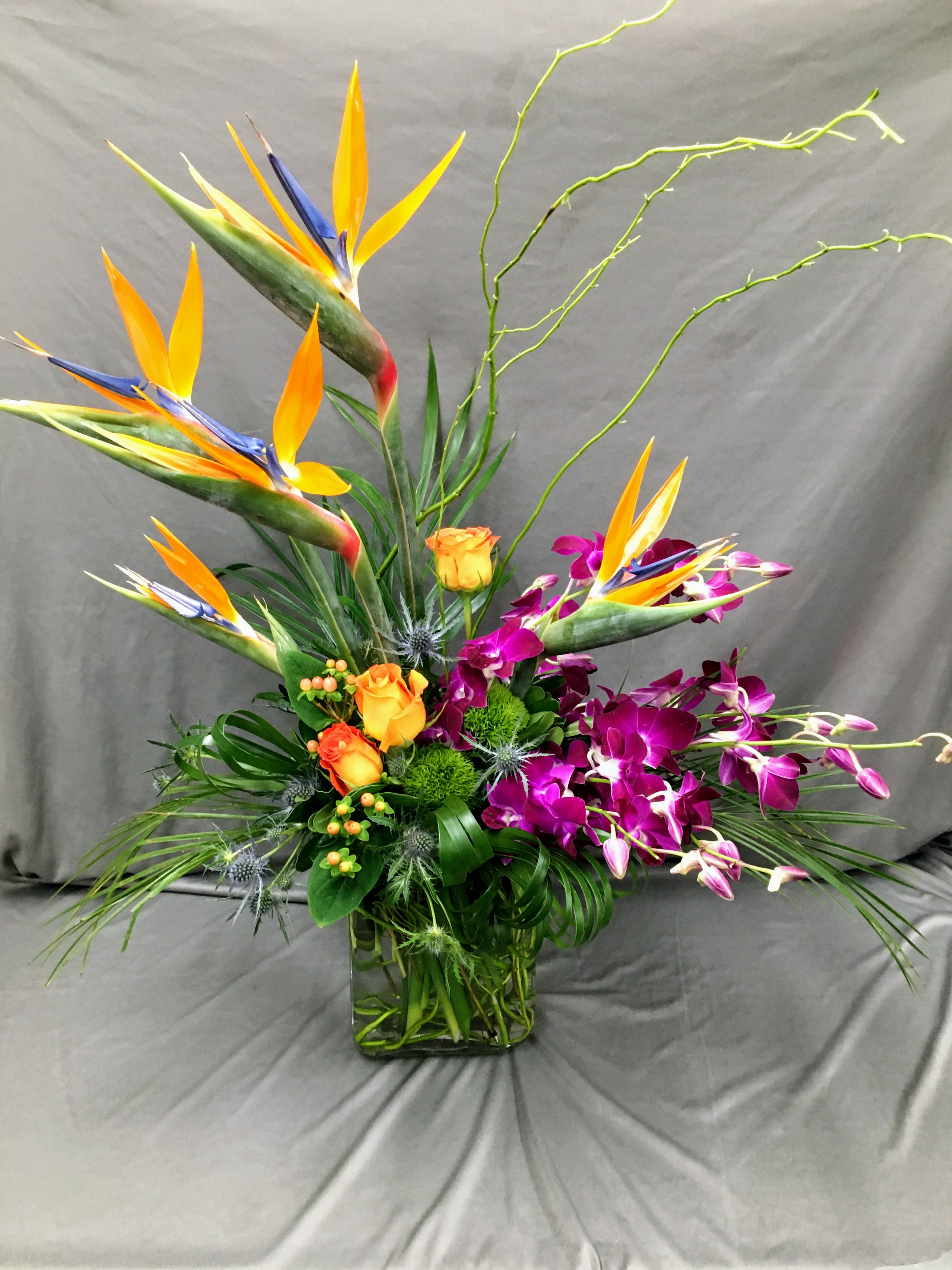 Tropical flower arrangement with bird of paradise, orchids, and roses in a glass vase