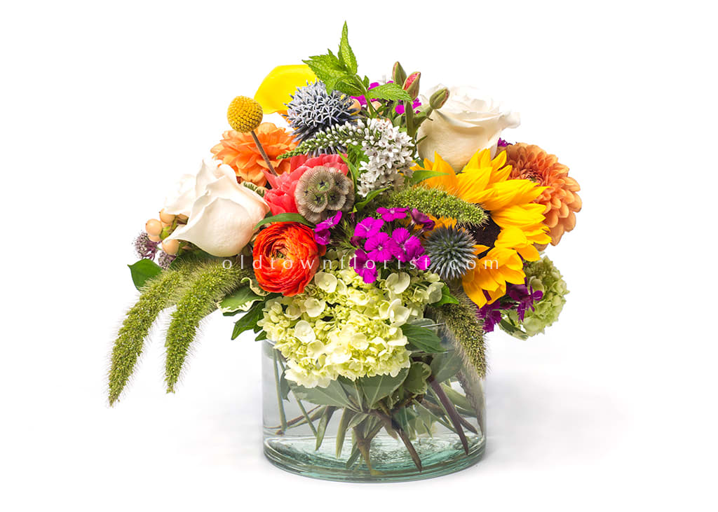 Mixed bouquet in a clear glass vase with sunflowers, roses, and hydrangeas