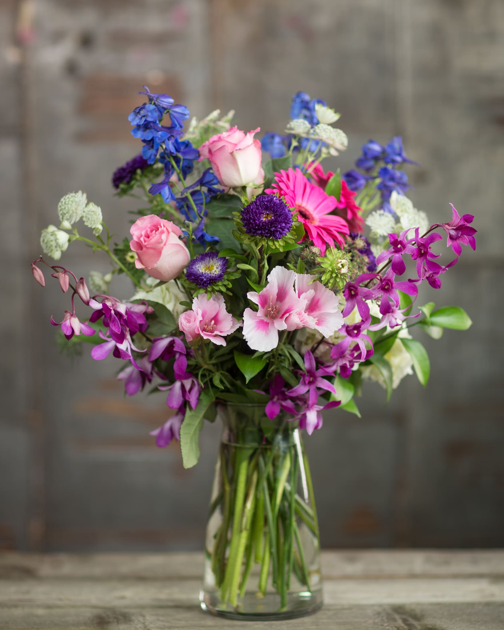 Mixed bouquet of pink, purple, and blue flowers in a clear glass vase