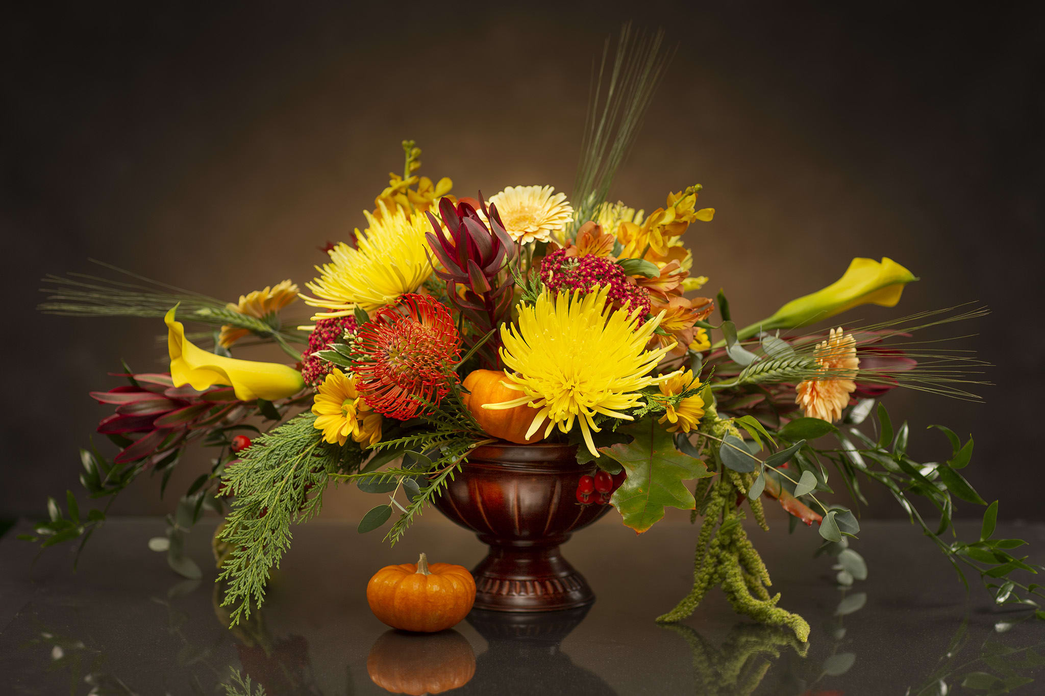 Autumn floral arrangement with yellow blooms in a dark vase and small pumpkins