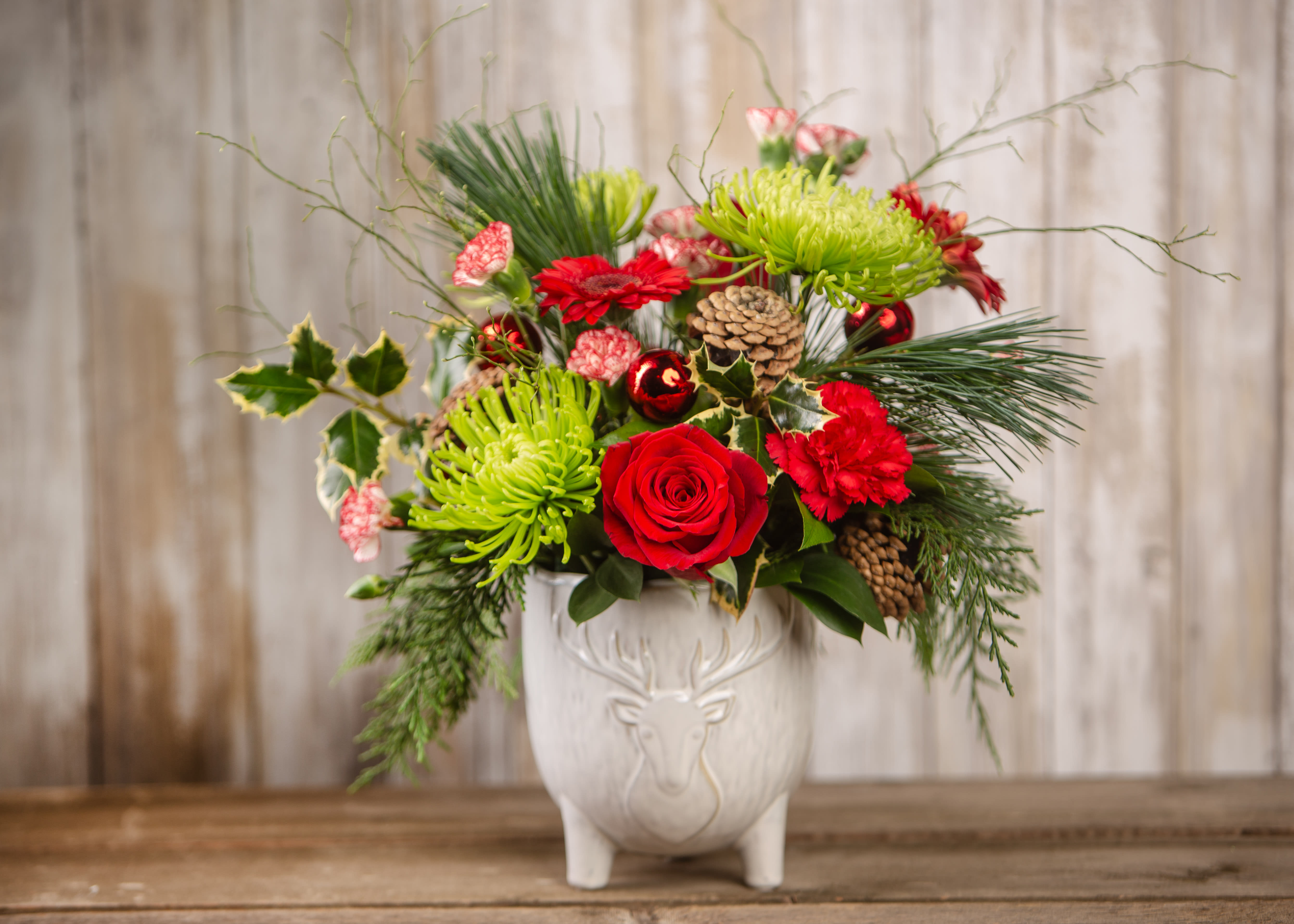 Holiday bouquet with red roses and green chrysanthemums in a white deer vase
