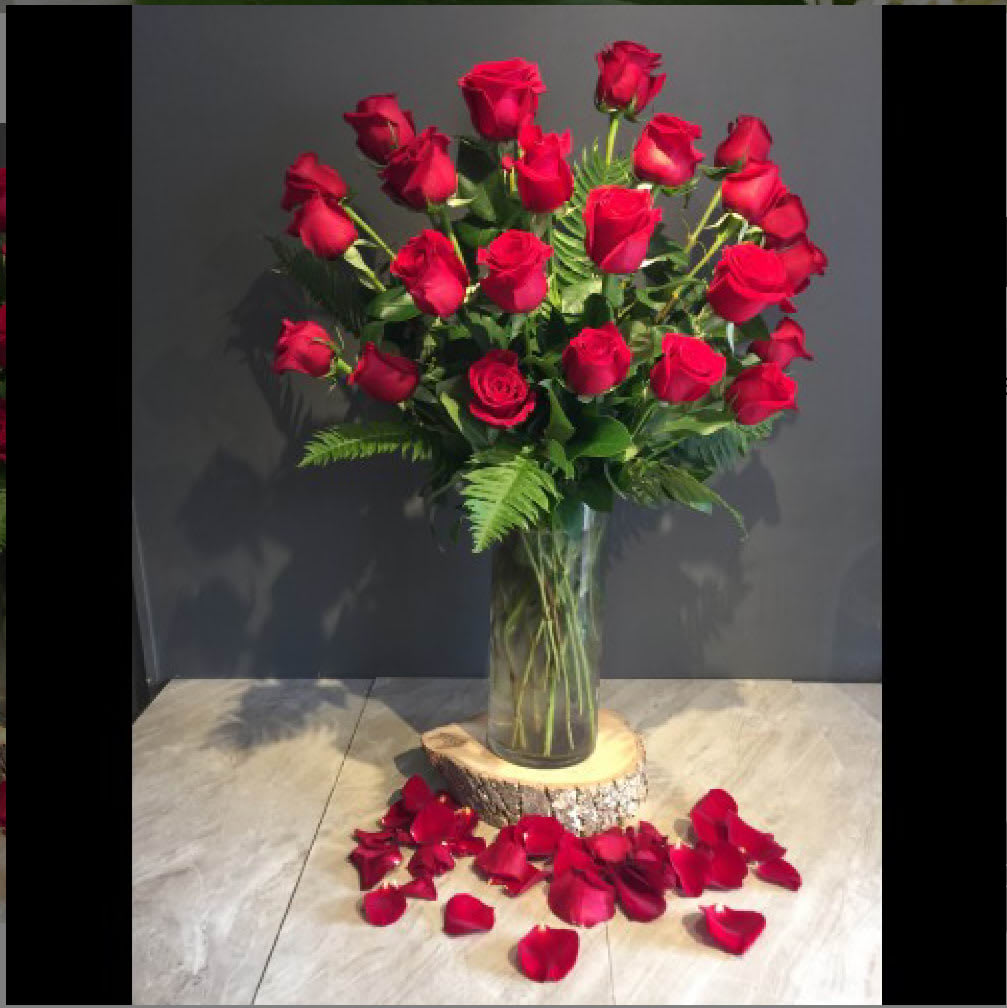 Tall bouquet of red roses in a clear glass vase with rose petals below